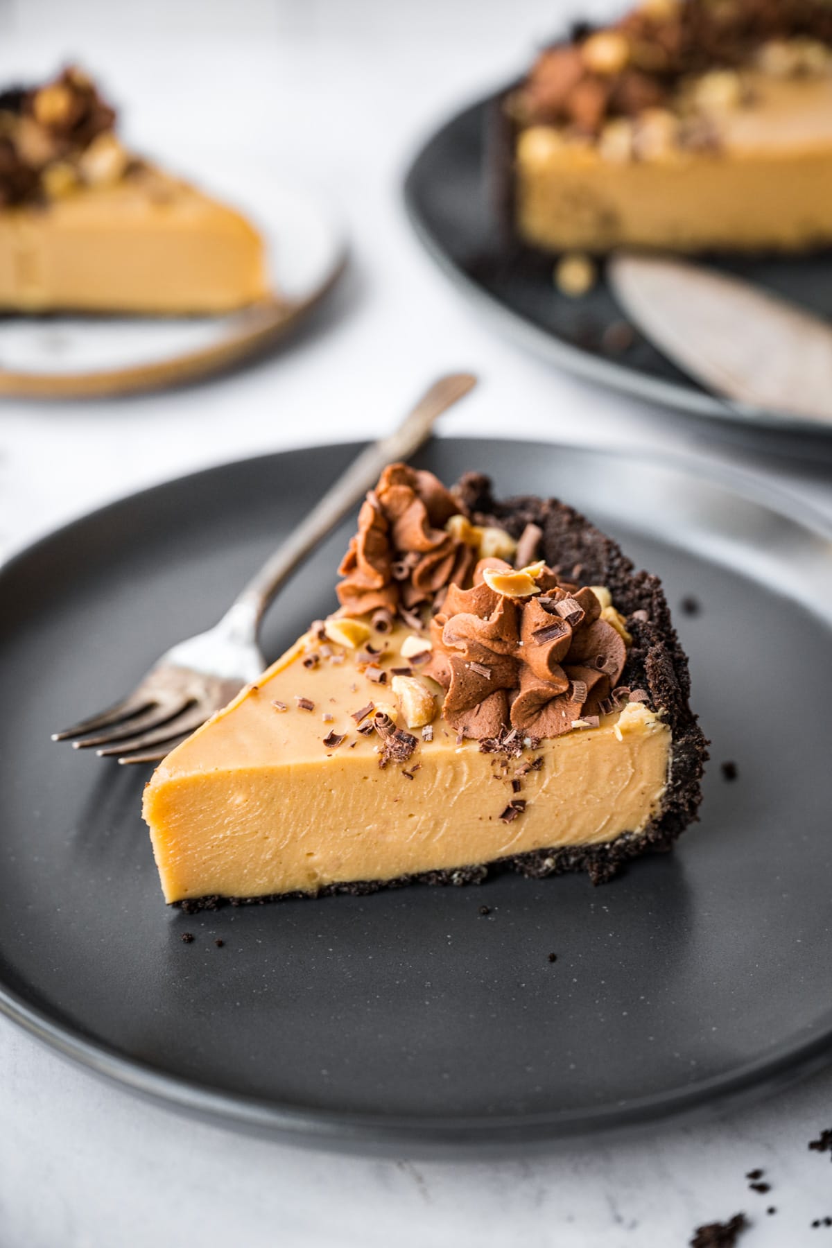 close up view of peanut butter pie with chocolate cookie crust on black plate. 