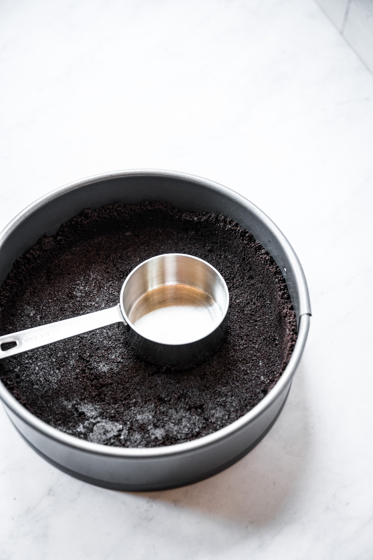 oreo pie crust in springform pan with measuring cup on top of crust. 