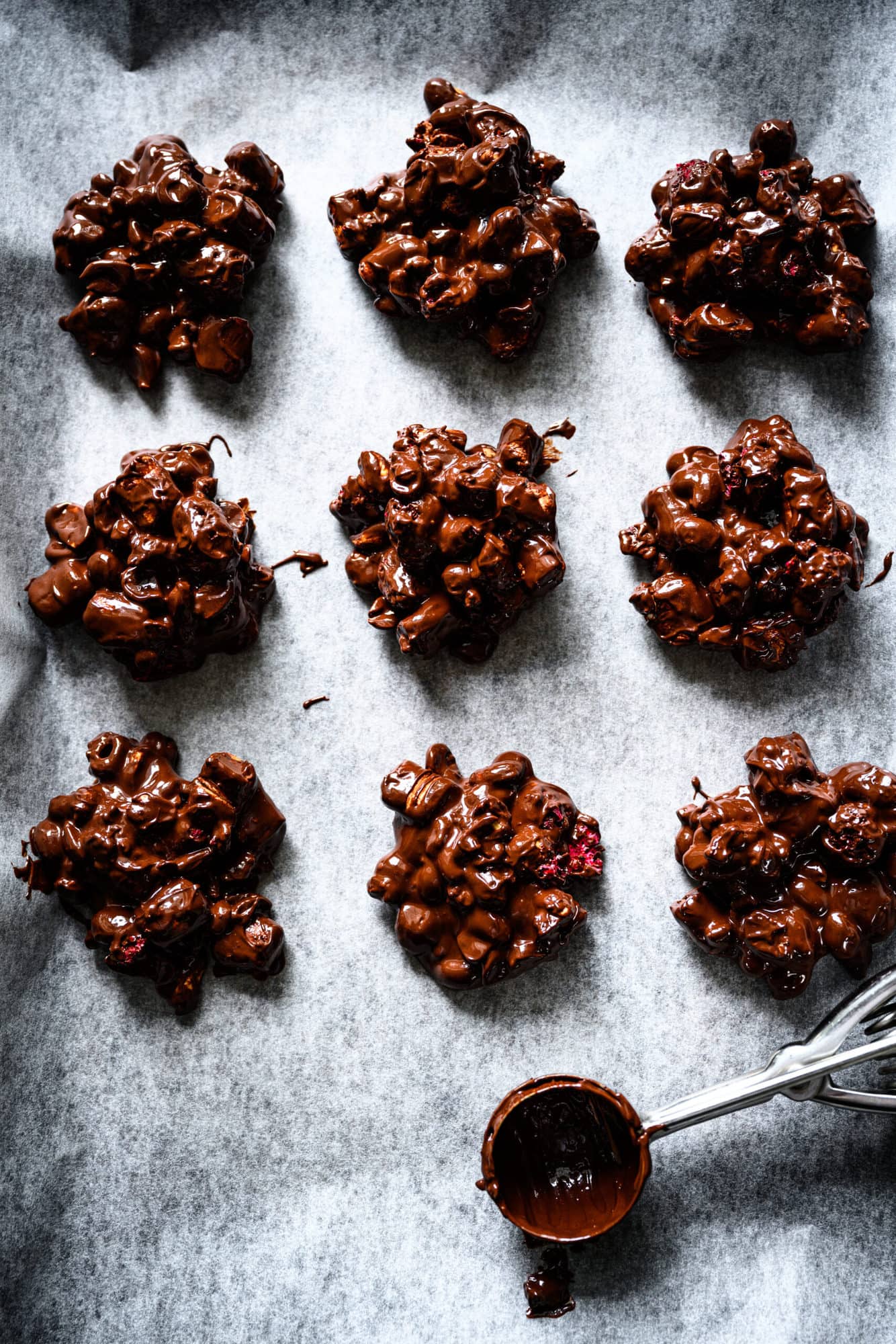 overhead view of vegan chocolate peanut marshmallow clusters on parchment paper with cookie scoop. 