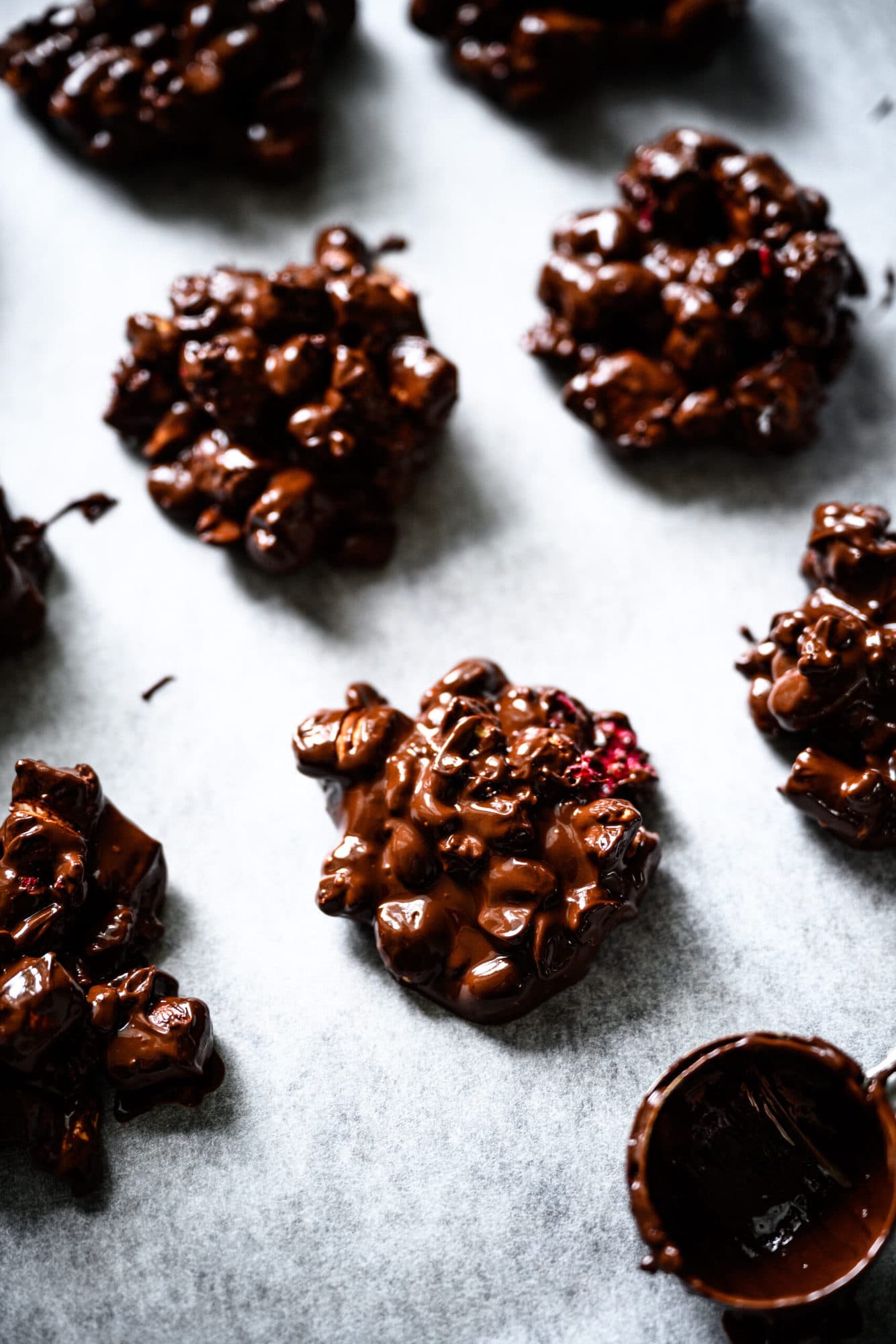 close up view of vegan chocolate peanut marshmallow clusters on parchment paper with cookie scoop. 