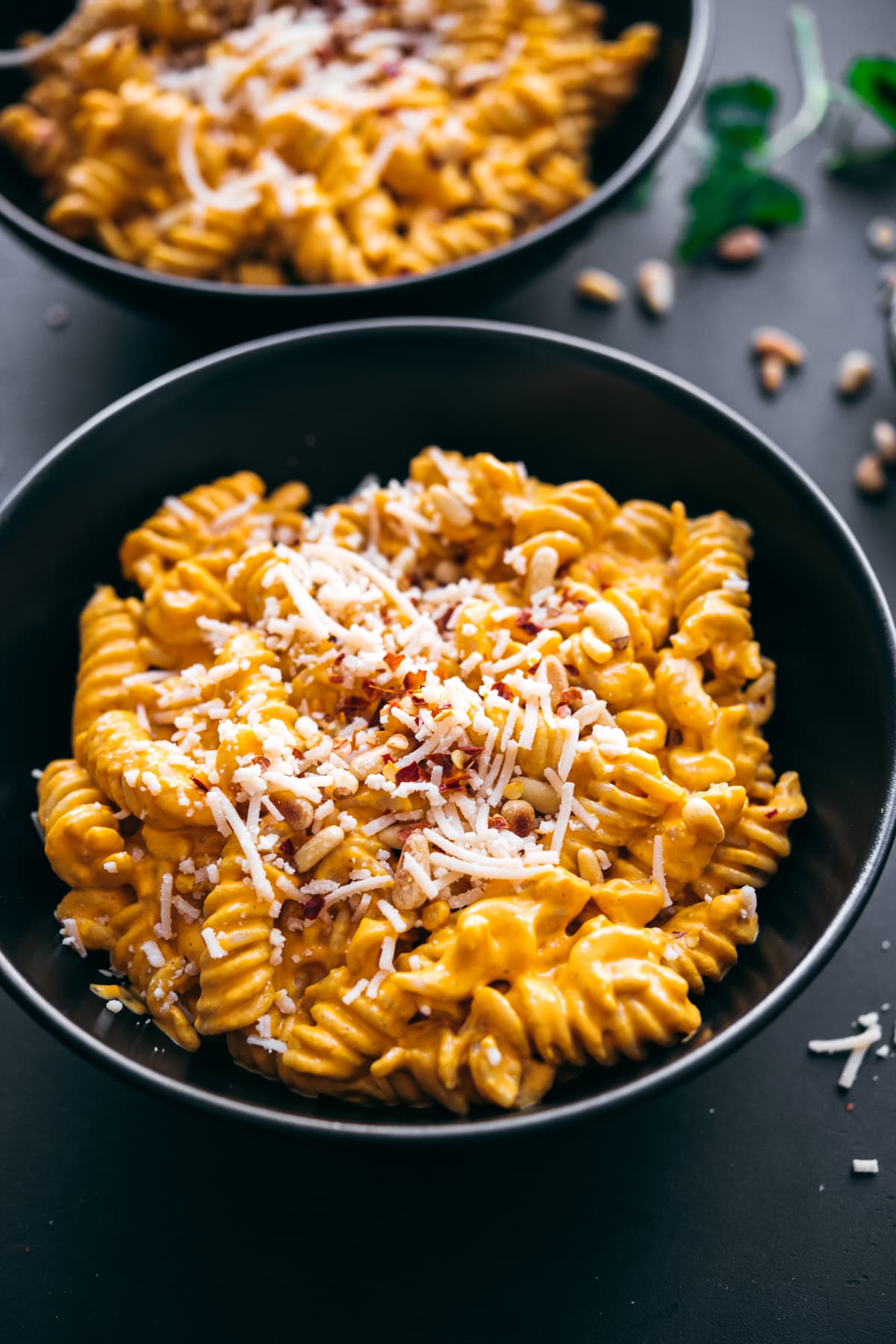 close up view of creamy vegan roasted red pepper pasta in black bowls topped with parmesan, pine nuts and red pepper flakes. 