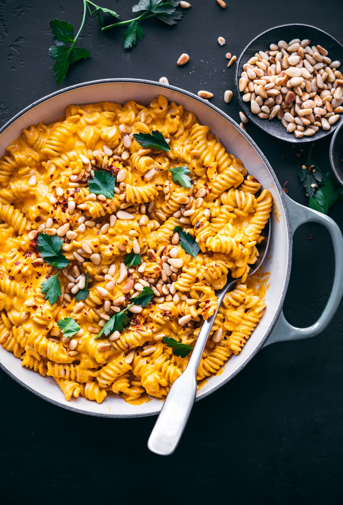 overhead view of creamy vegan roasted red pepper pasta in pan topped with pine nuts and red pepper flakes. 