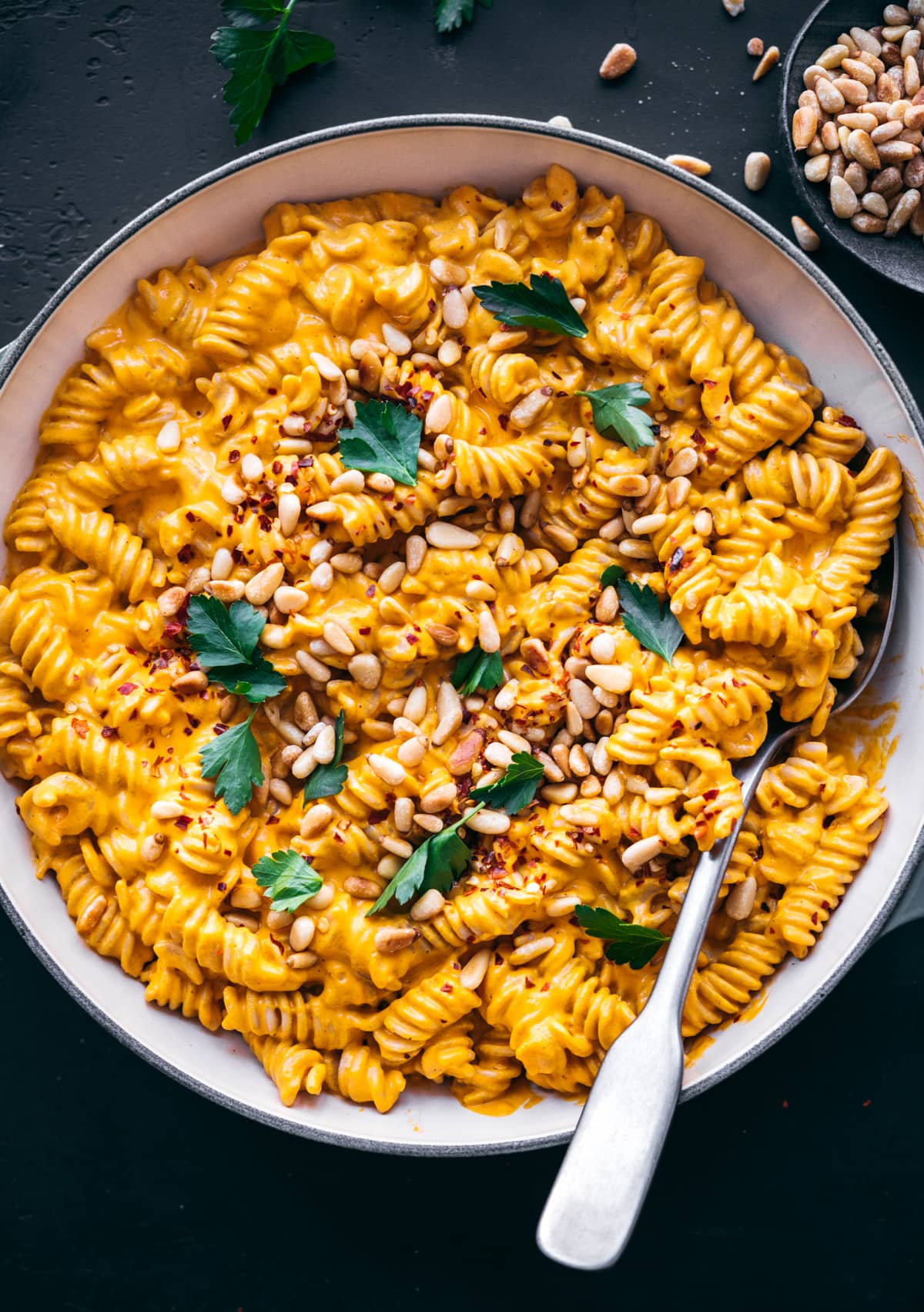 overhead view of creamy vegan roasted red pepper pasta in pan topped with pine nuts and red pepper flakes. 