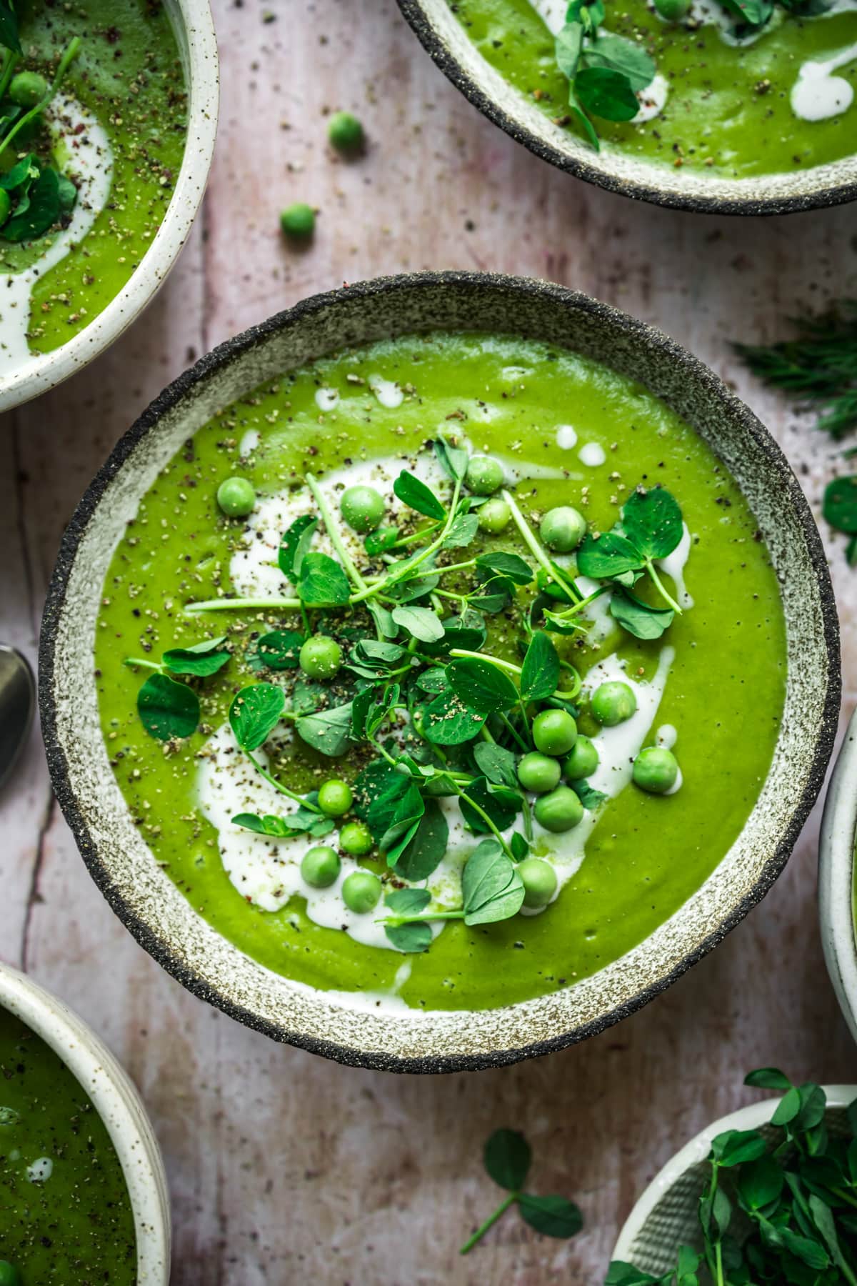 overhead view of vegan asparagus soup with peas in rustic bowl with cream swirl and microgreen garnish.