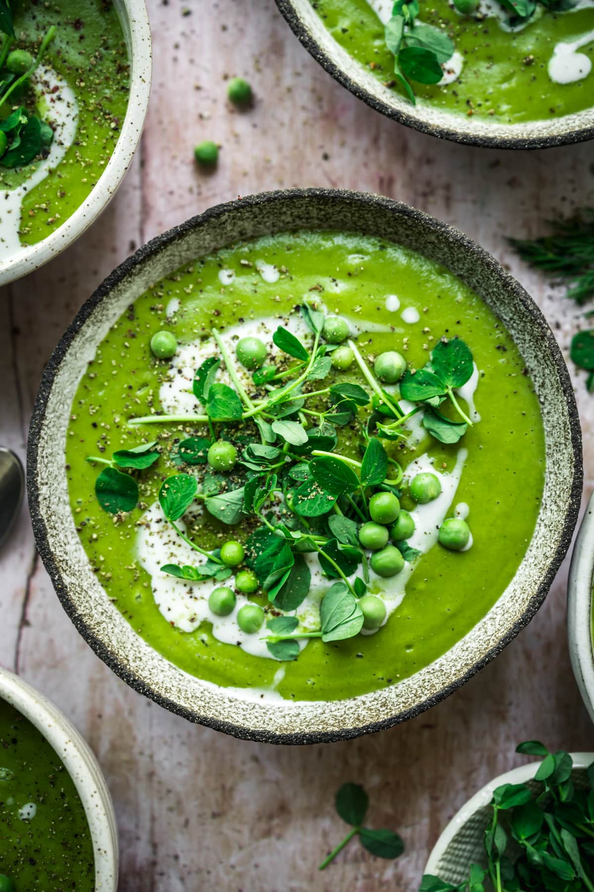 overhead view of vegan asparagus soup with peas in rustic bowl with cream swirl and microgreen garnish. 