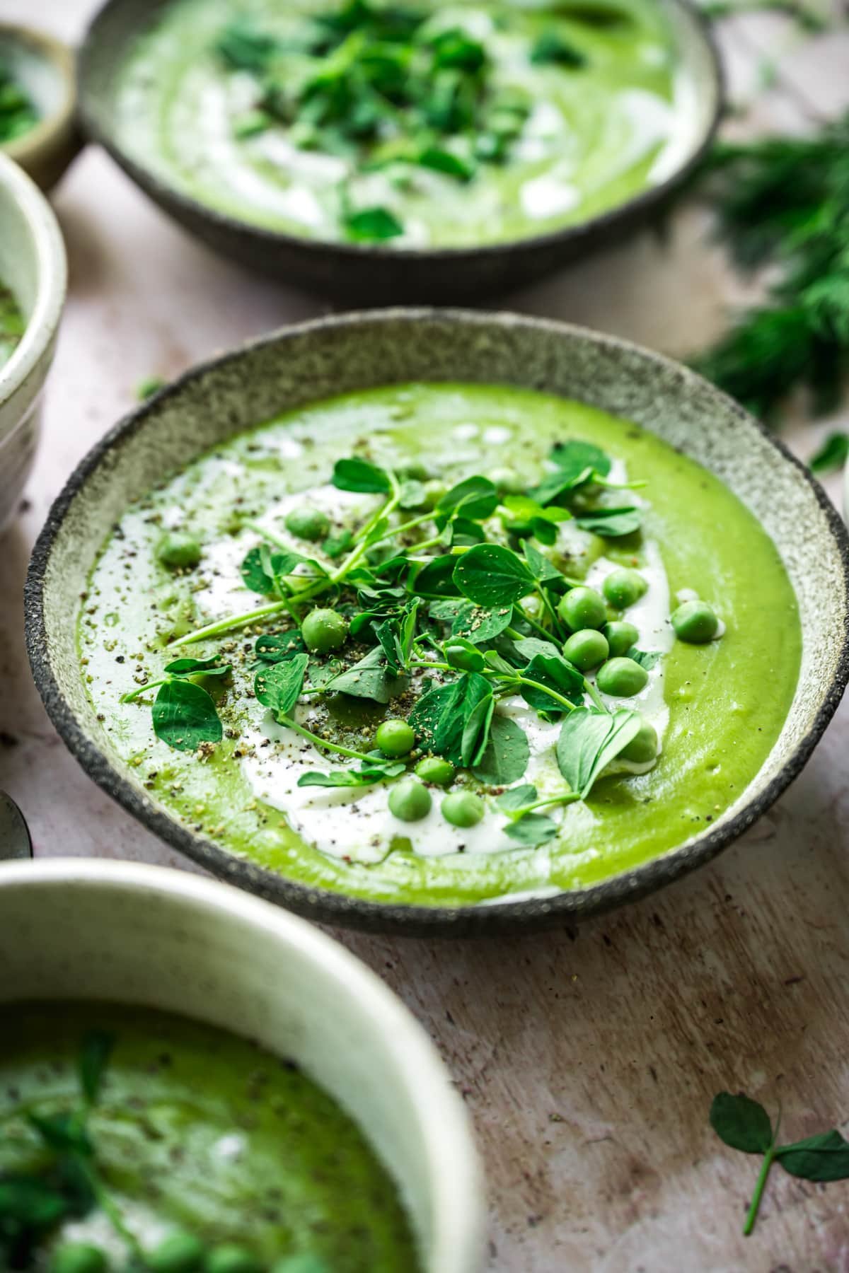close up view of vegan asparagus soup with peas in rustic bowl with cream swirl and microgreen garnish. 