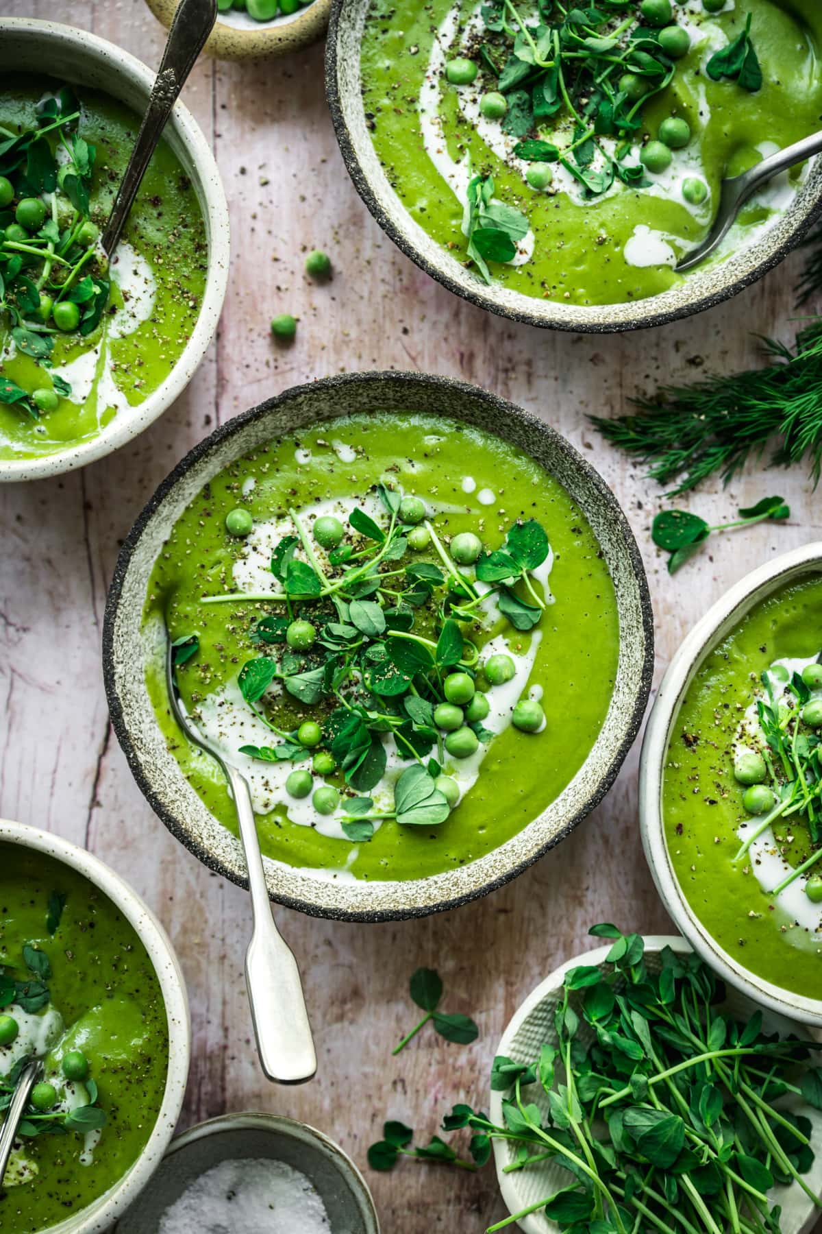 overhead view of vegan asparagus soup with peas in rustic bowl with cream swirl and microgreen garnish. 