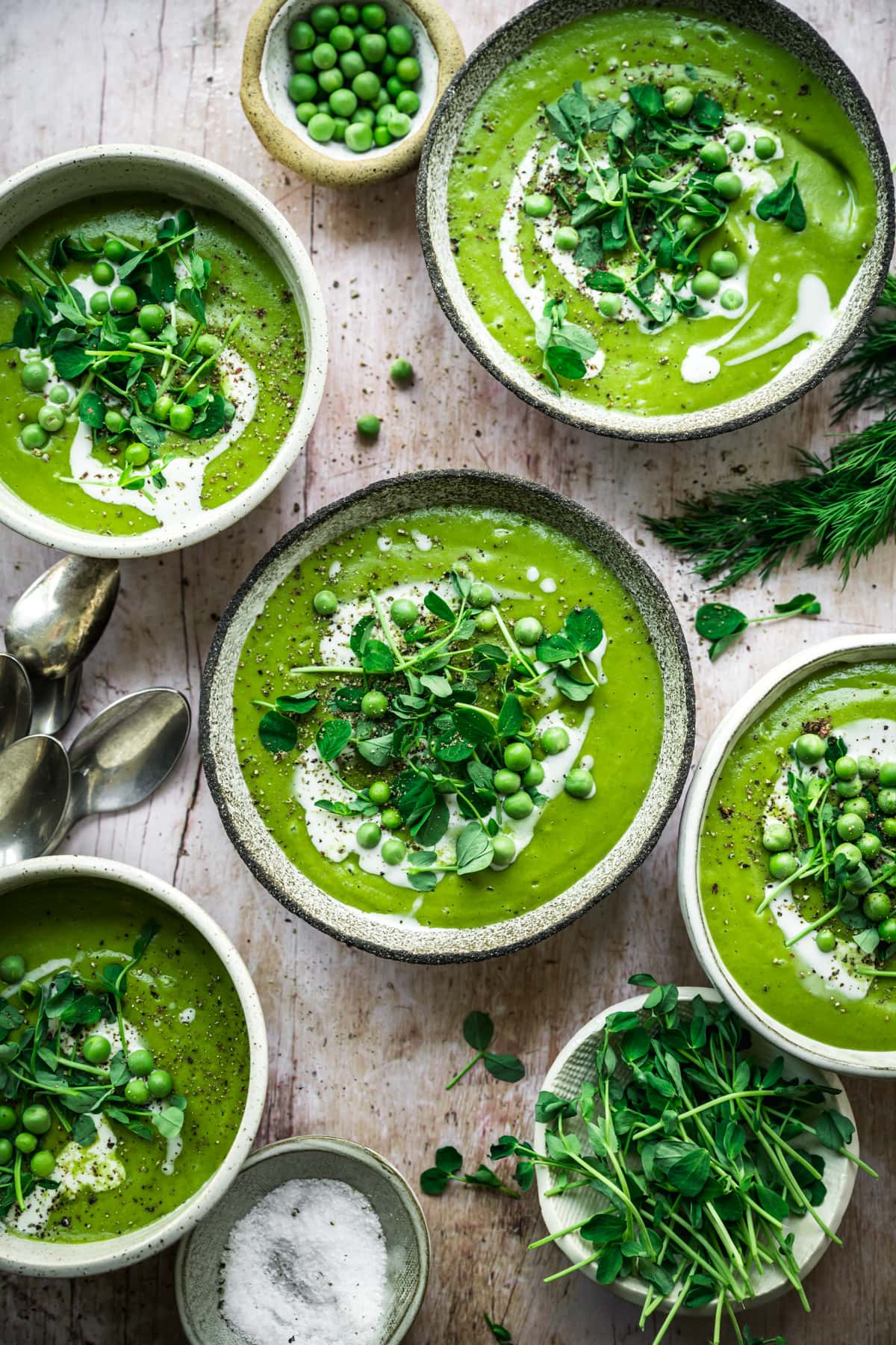 overhead view of vegan asparagus soup with peas in rustic bowl with cream swirl and microgreen garnish.