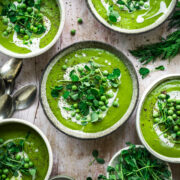 overhead view of vegan asparagus soup with peas in rustic bowl with cream swirl and microgreen garnish.