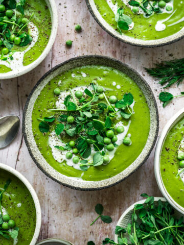 overhead view of vegan asparagus soup with peas in rustic bowl with cream swirl and microgreen garnish.