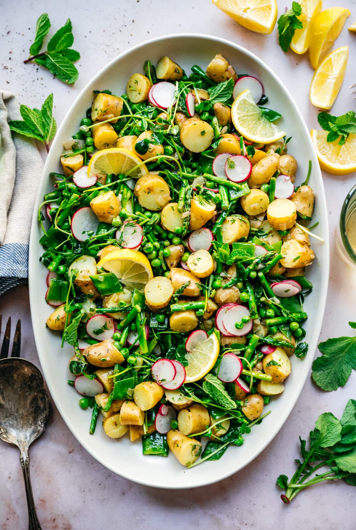overhead view of asparagus potato salad with peas and radishes on a large white platter. 