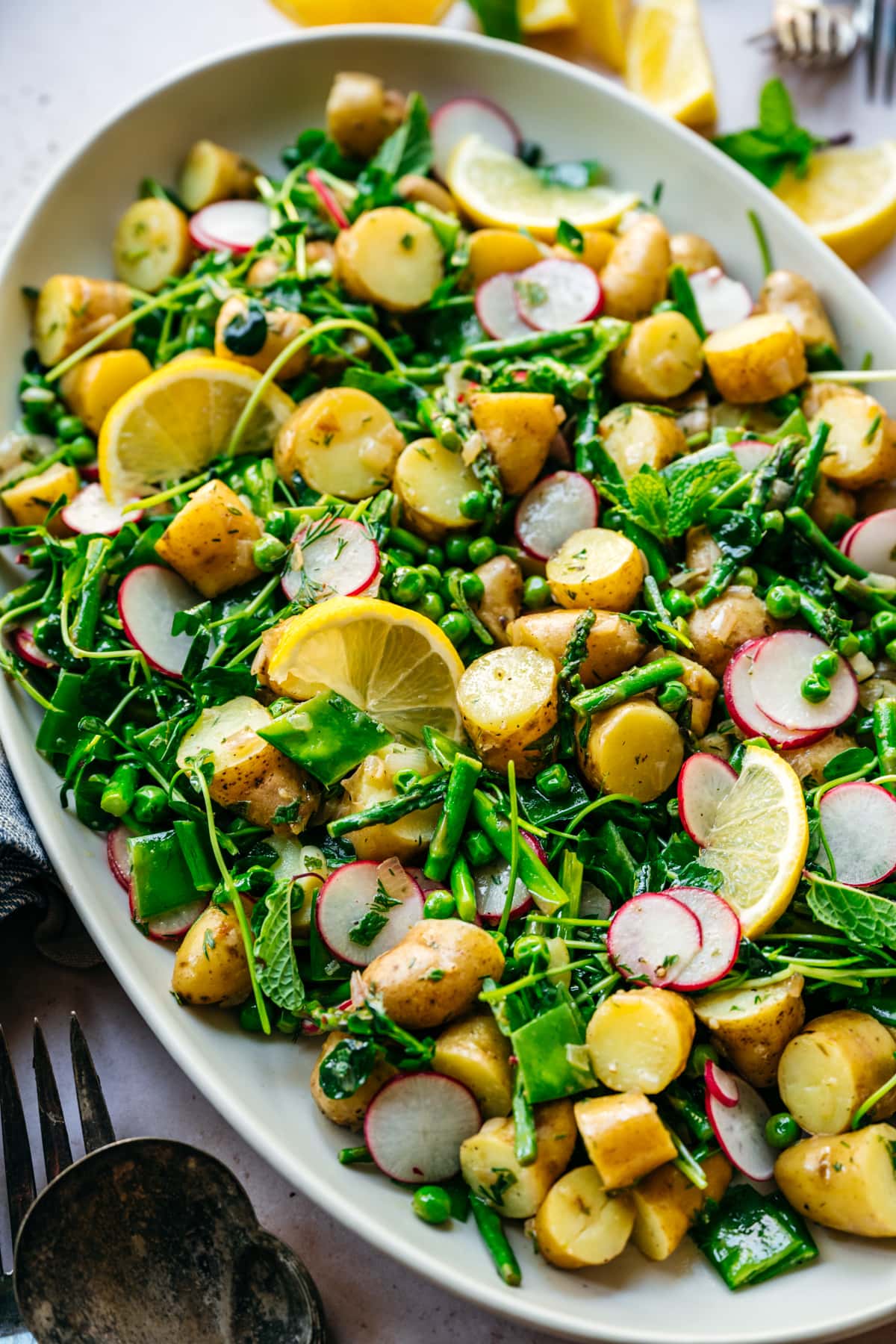 close up view of asparagus potato salad with peas and radishes on a large white platter. 