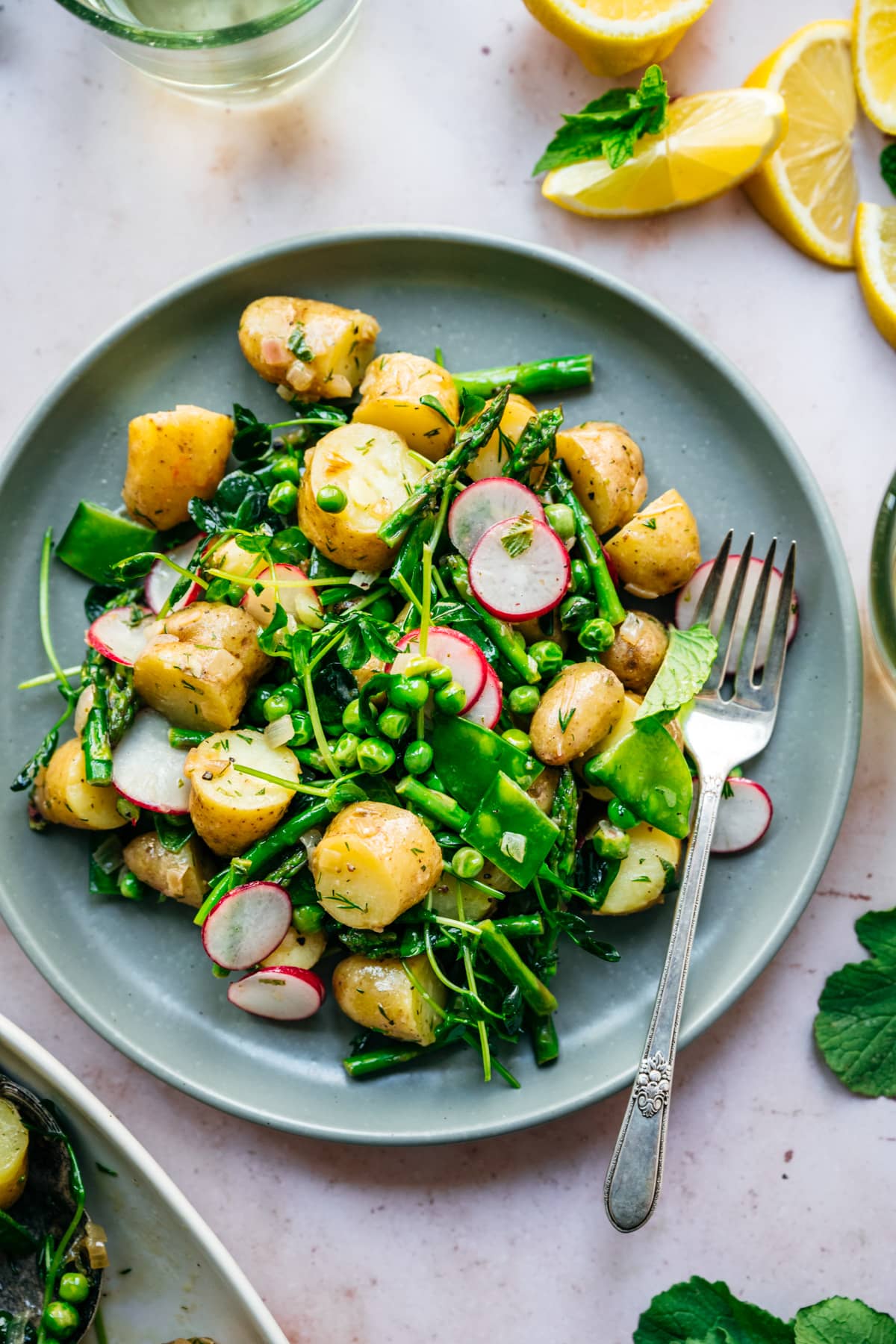 overhead view of asparagus potato salad with peas and radishes on a blue plate with fork.