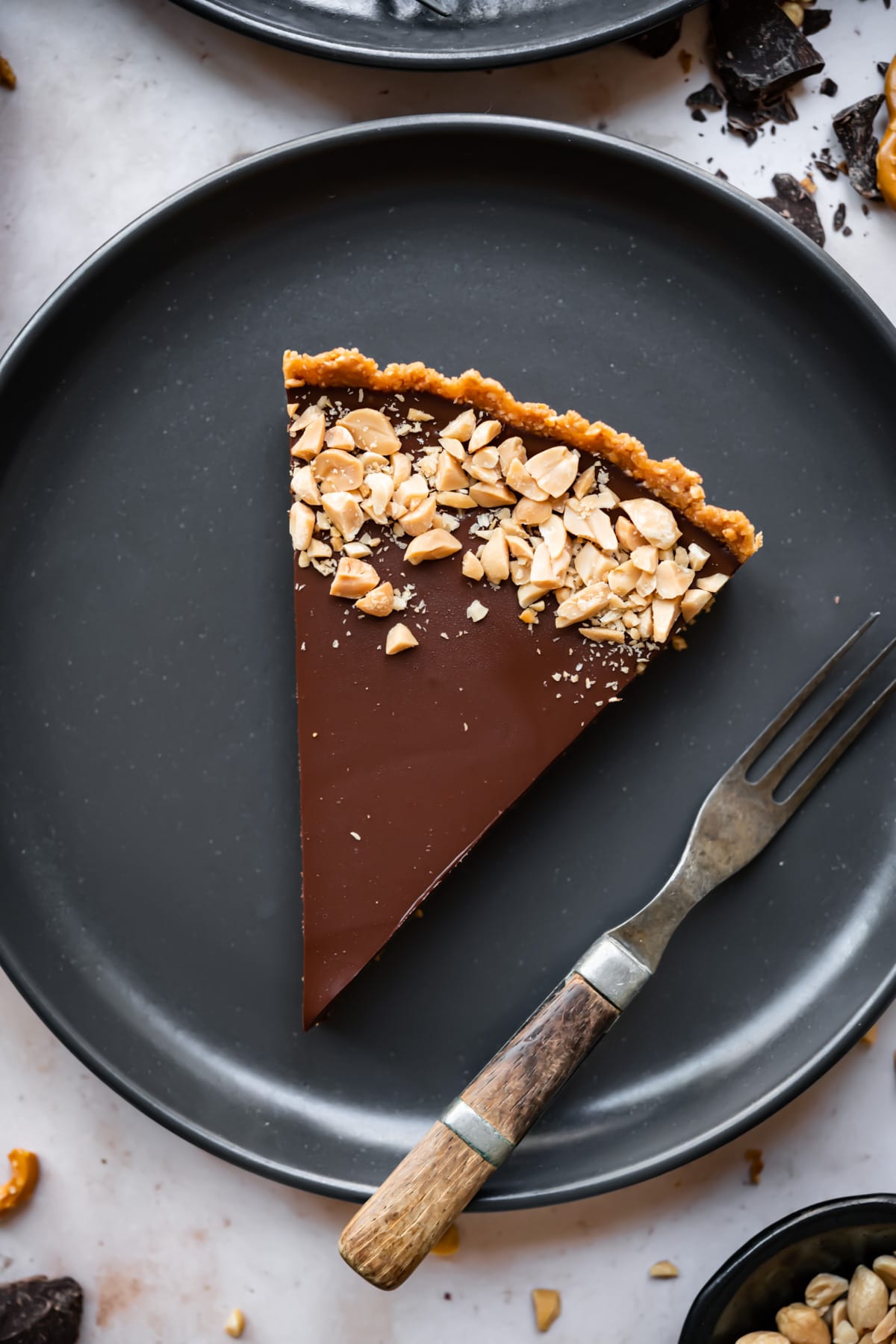 overhead view of slice of chocolate peanut butter pretzel tart on a black plate. 