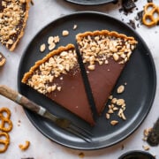 overhead view of 2 slices of chocolate peanut butter pretzel tart on a black plate.