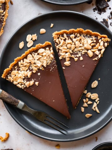 overhead view of 2 slices of chocolate peanut butter pretzel tart on a black plate.