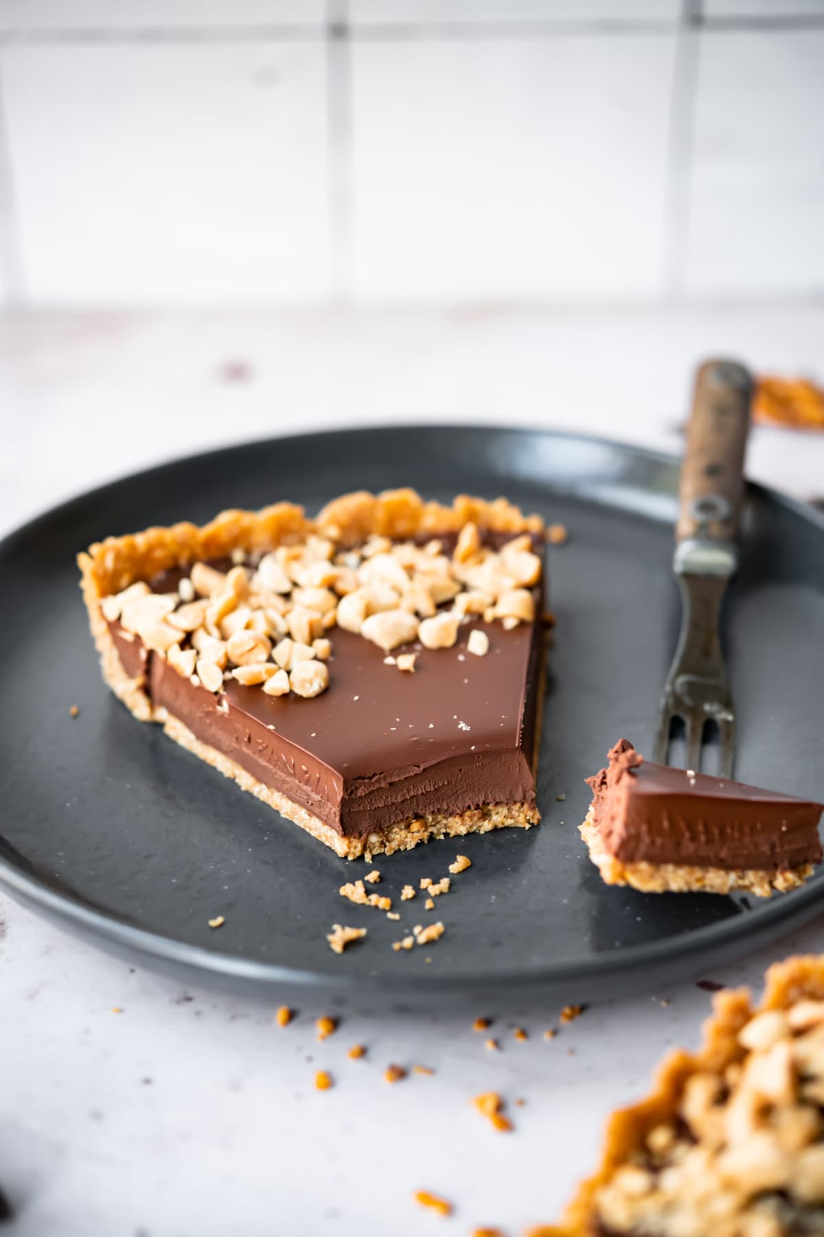 close up side view of a slice of chocolate peanut butter pretzel tart on a black plate. 