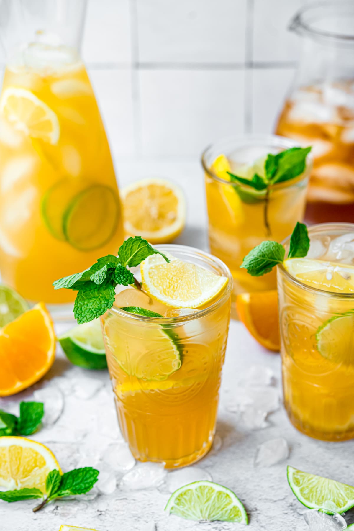 Three glasses of long island iced tea with a pitcher in the background.