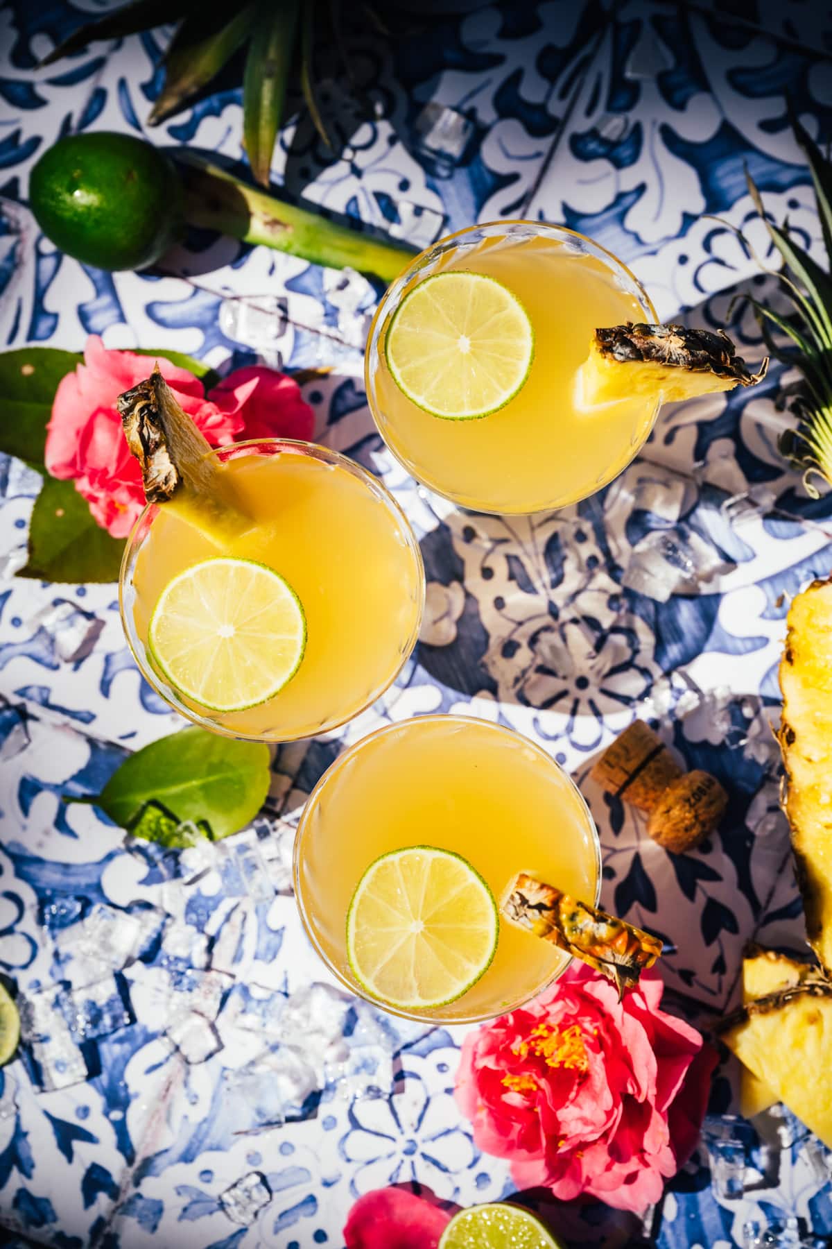 overhead view of pineapple mimosas on blue tile backdrop. 