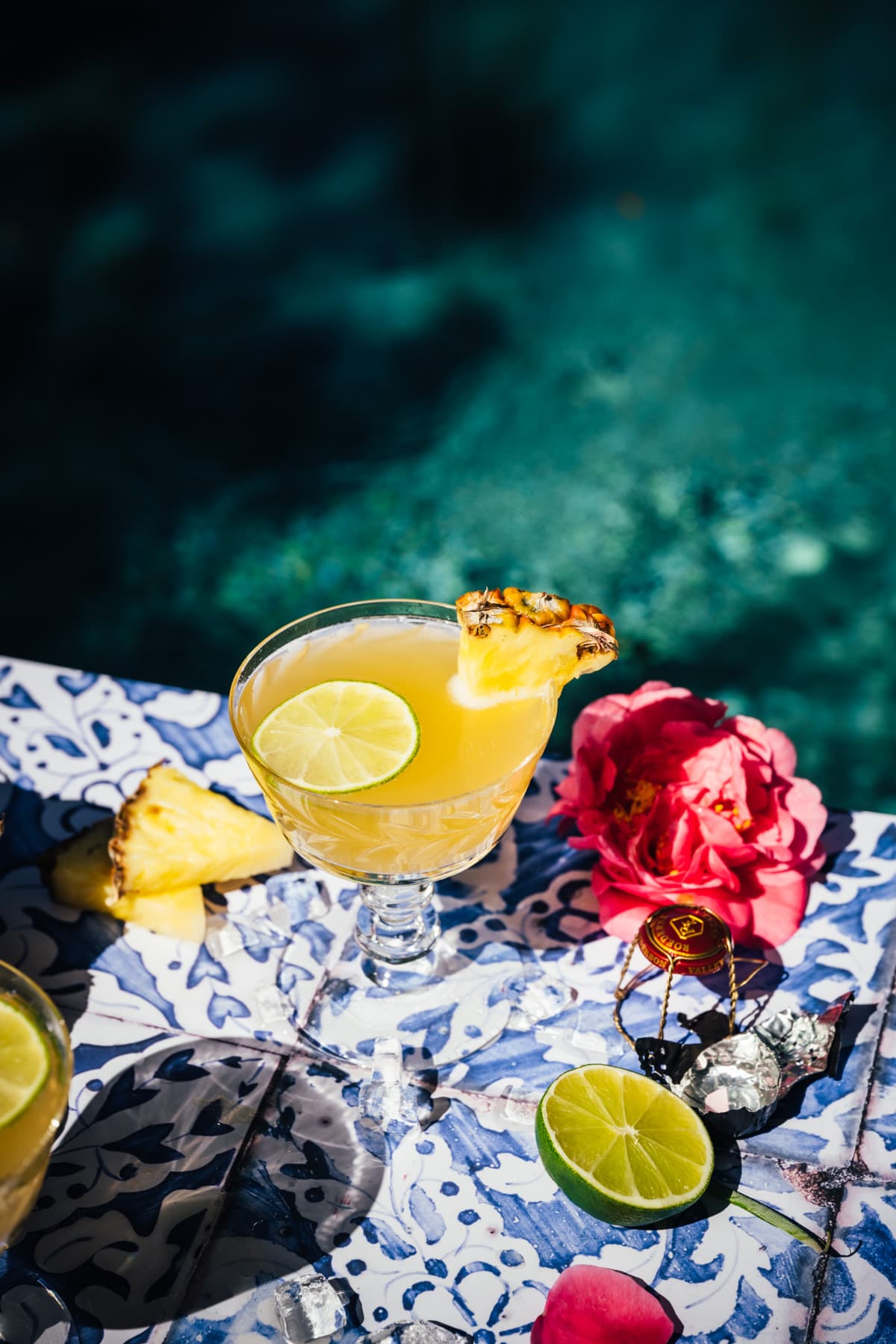 overhead view of pineapple mimosa on blue tile with pool in background. 