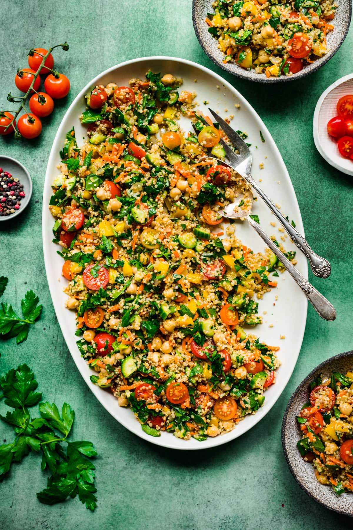 overhead view of quinoa chickpea vegetable salad on a large white platter on green backdrop. 