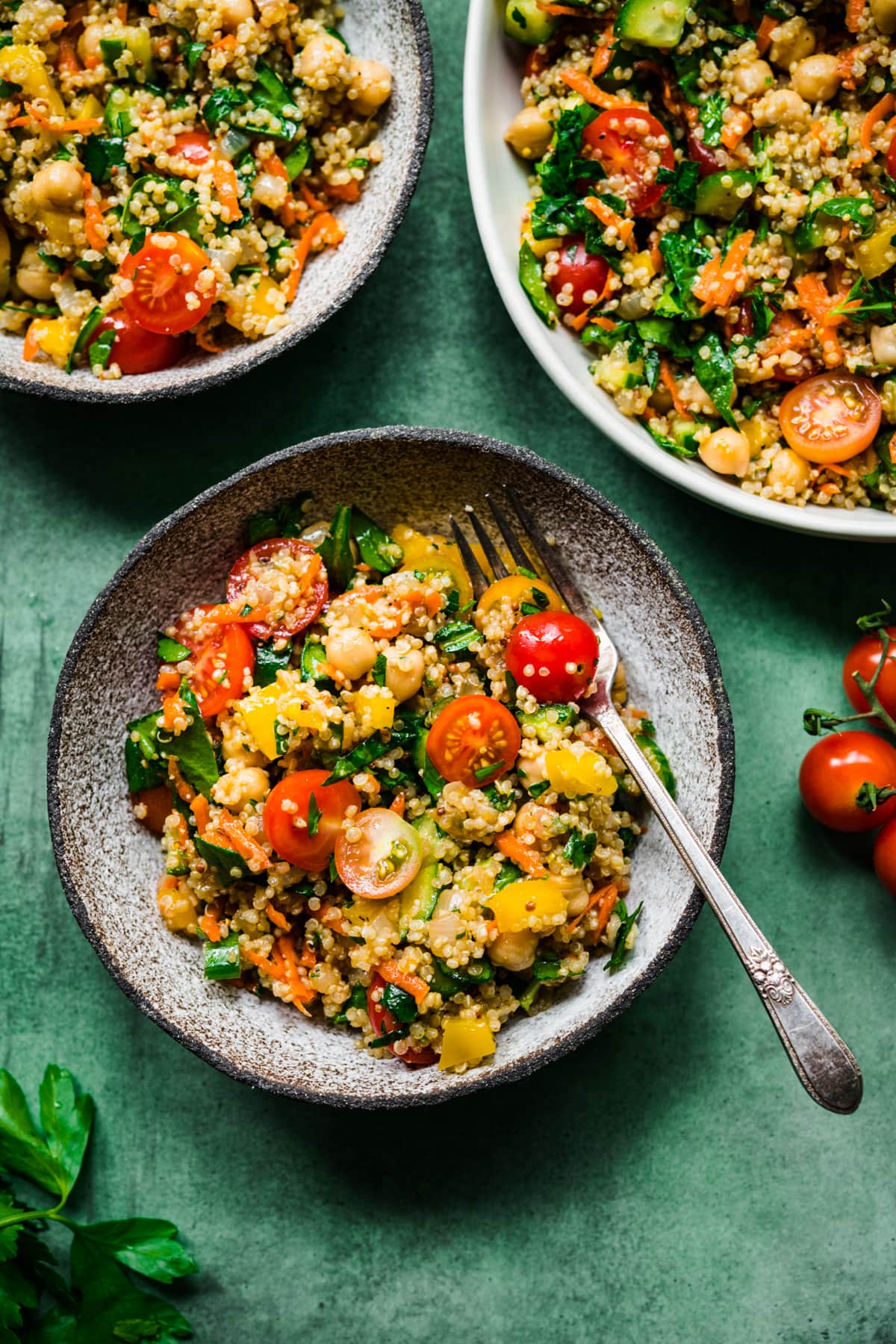 overhead view of vegan quinoa chickpea salad with vegetables in a bowl on green backdrop. 