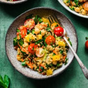 overhead view of vegan quinoa chickpea salad with vegetables in a bowl on green backdrop.