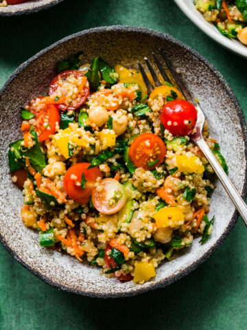 overhead view of vegan quinoa chickpea salad with vegetables in a bowl on green backdrop.