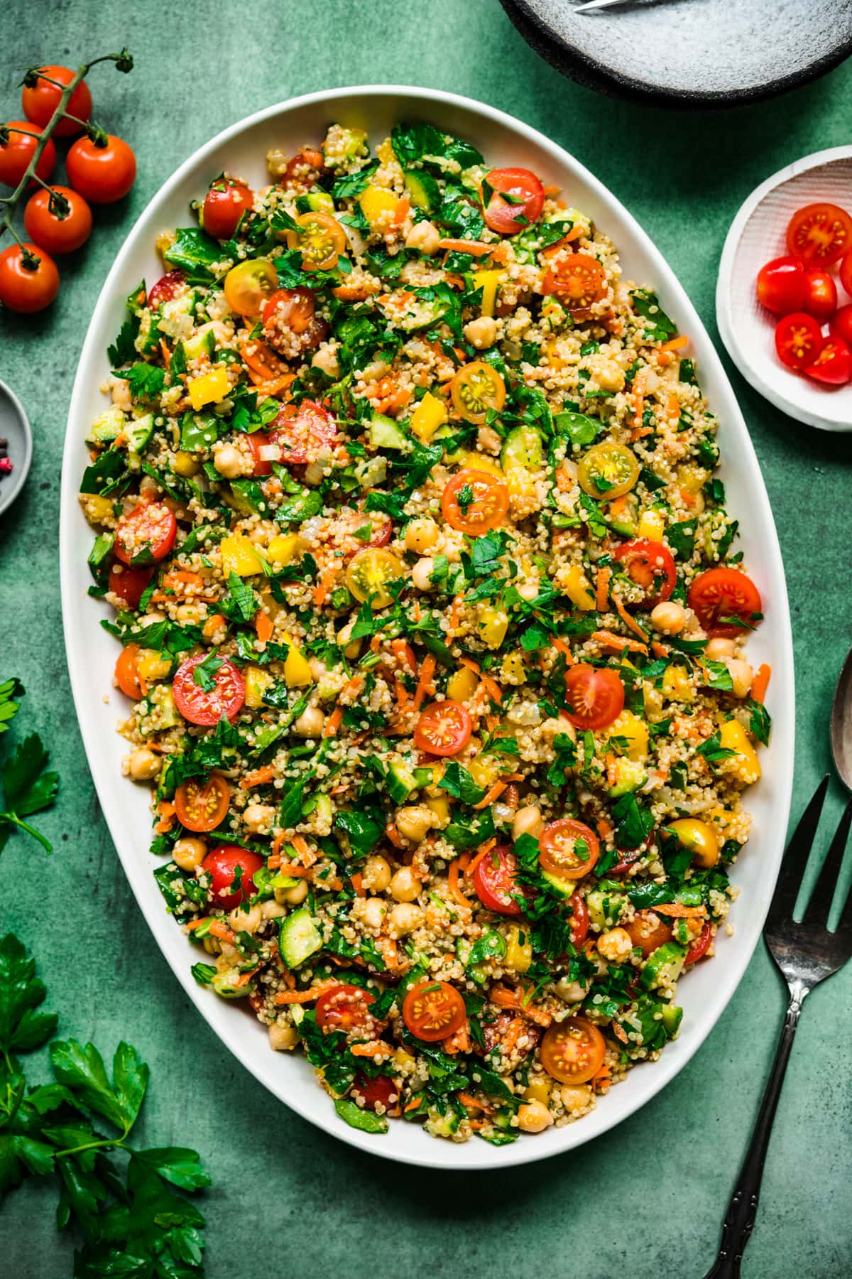 overhead view of quinoa chickpea vegetable salad on a large white platter on green backdrop. 