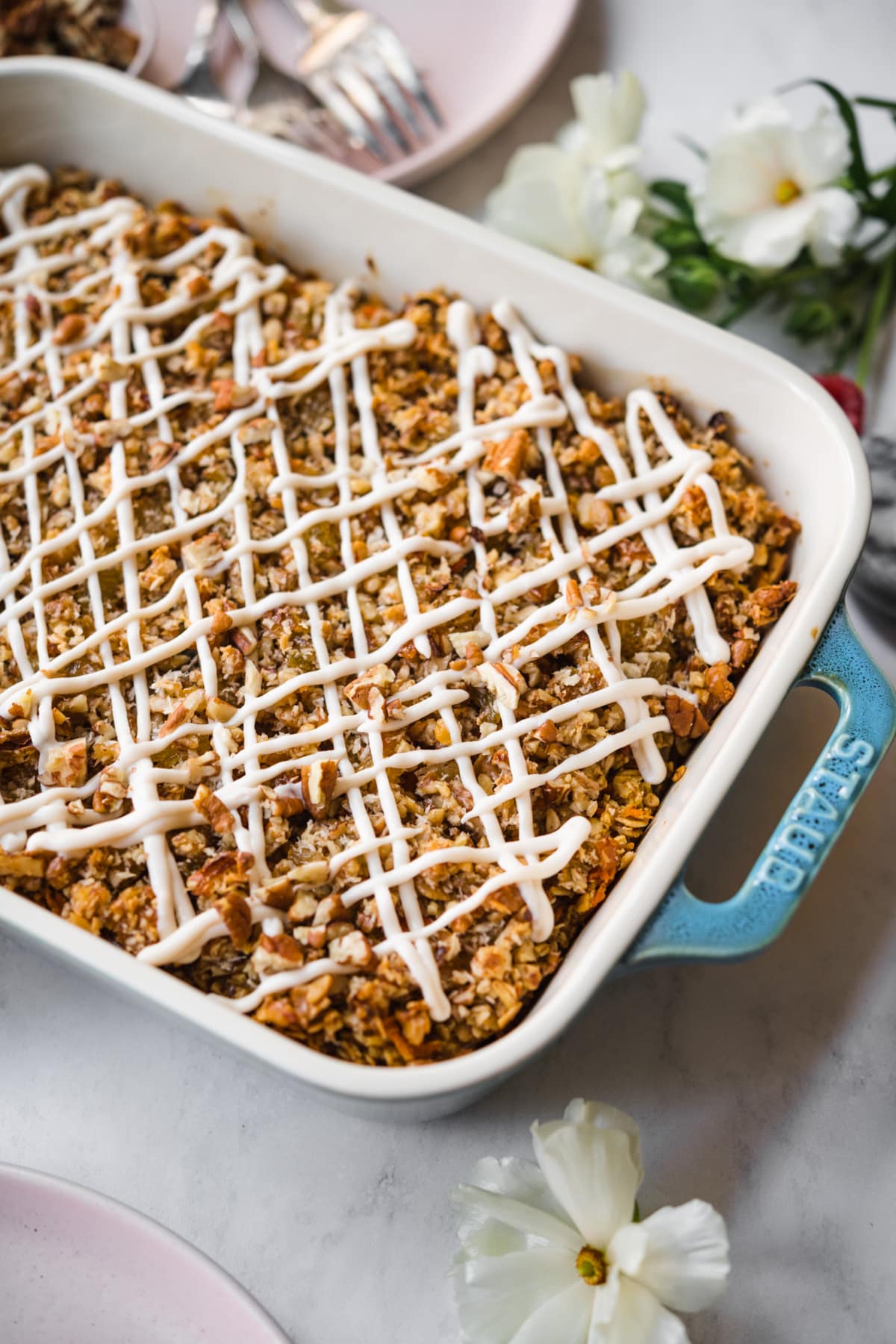 close up view of vegan carrot cake baked in a blue baking dish with cream cheese glaze. 