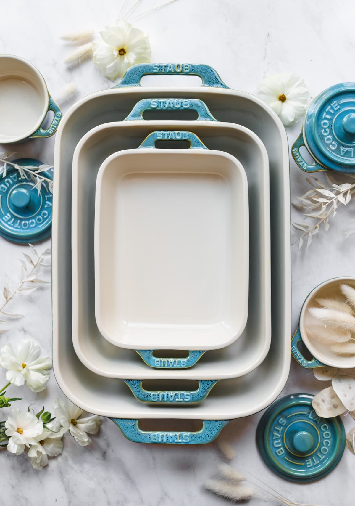 overhead view of Staub turquoise ceramic baking dishes and cocottes on marble surface. 