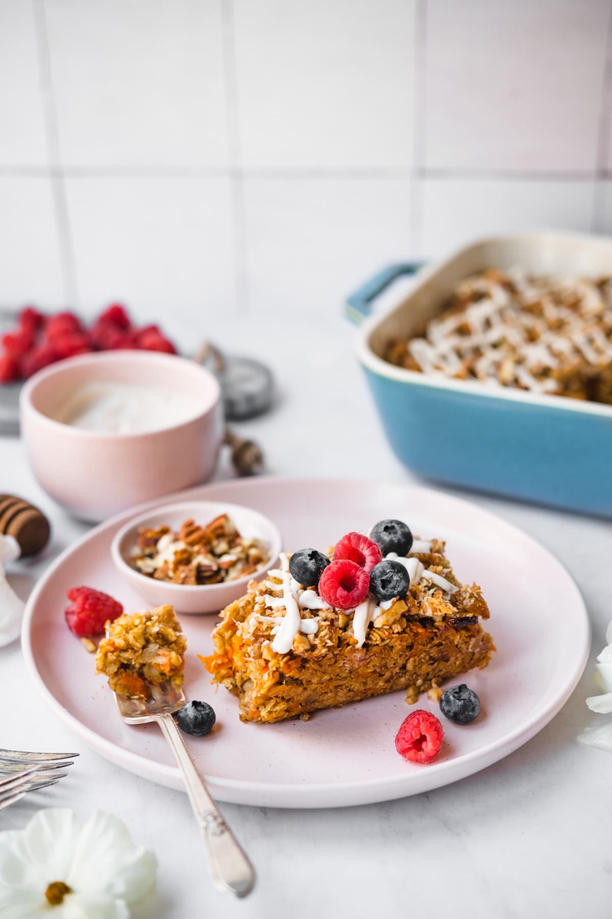 slice of vegan carrot cake baked oatmeal with fresh berries on top on a pink plate. 