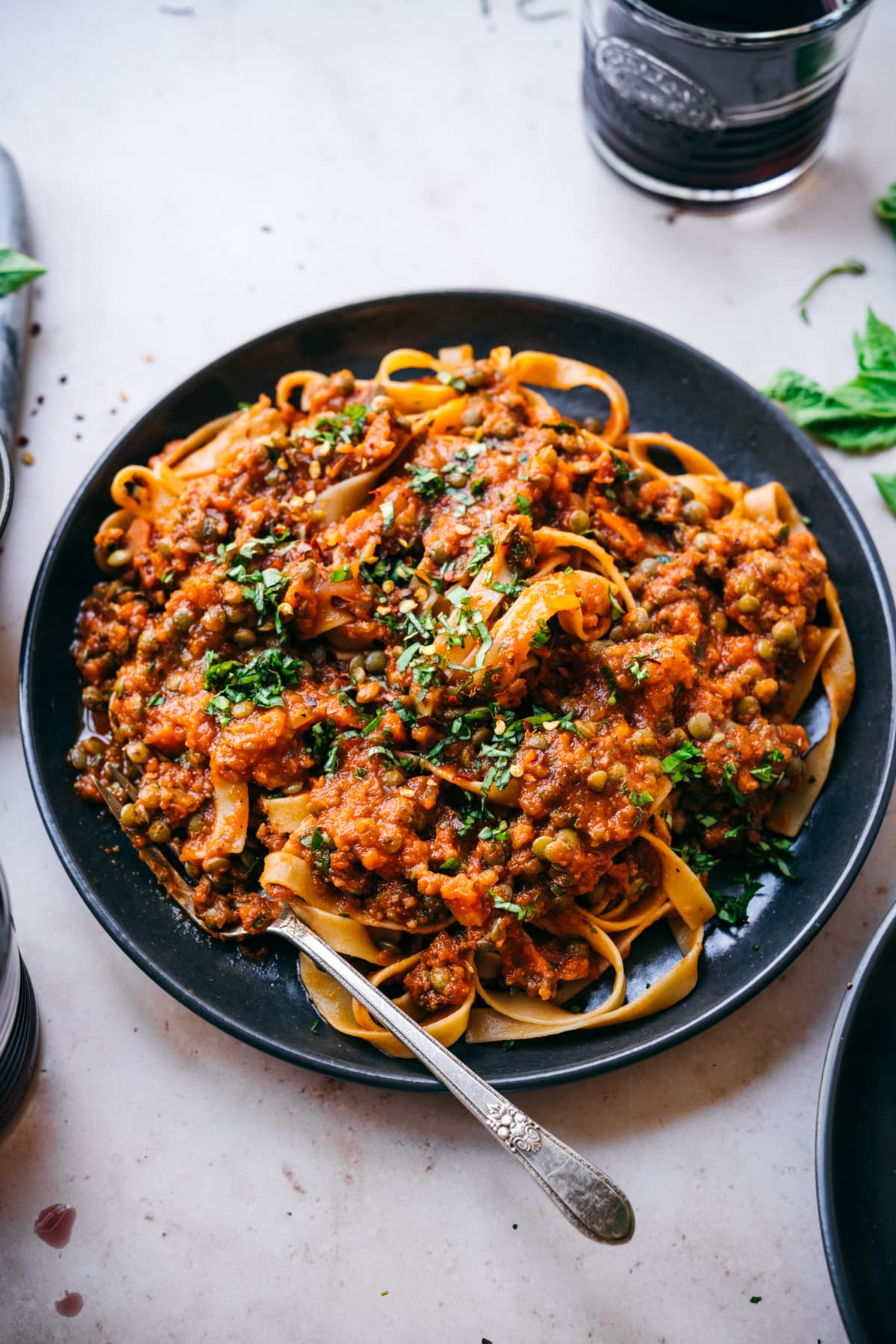 close up view of vegan lentil bolognese sauce over pasta on black plate with fork. 