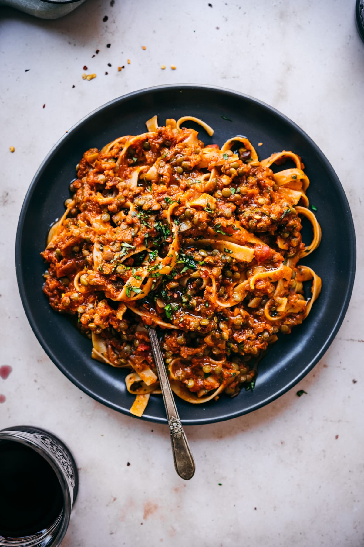 overhead view of vegan lentil bolognese sauce over pasta on black plate with fork. 