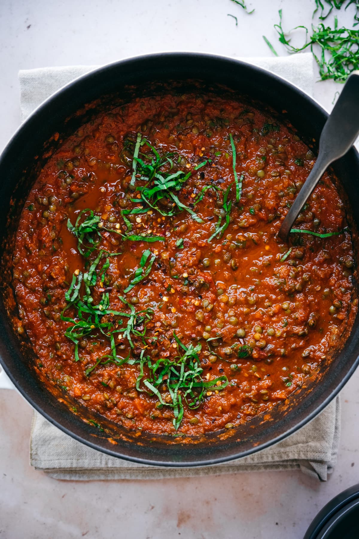 overhead view of vegan lentil bolognese sauce in large pot topped with fresh basil. 