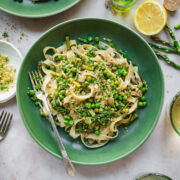 close up view of vegan spring vegetable pasta plated in a green bowl with breadcrumb topping.