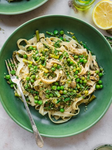 close up view of vegan spring vegetable pasta plated in a green bowl with breadcrumb topping.