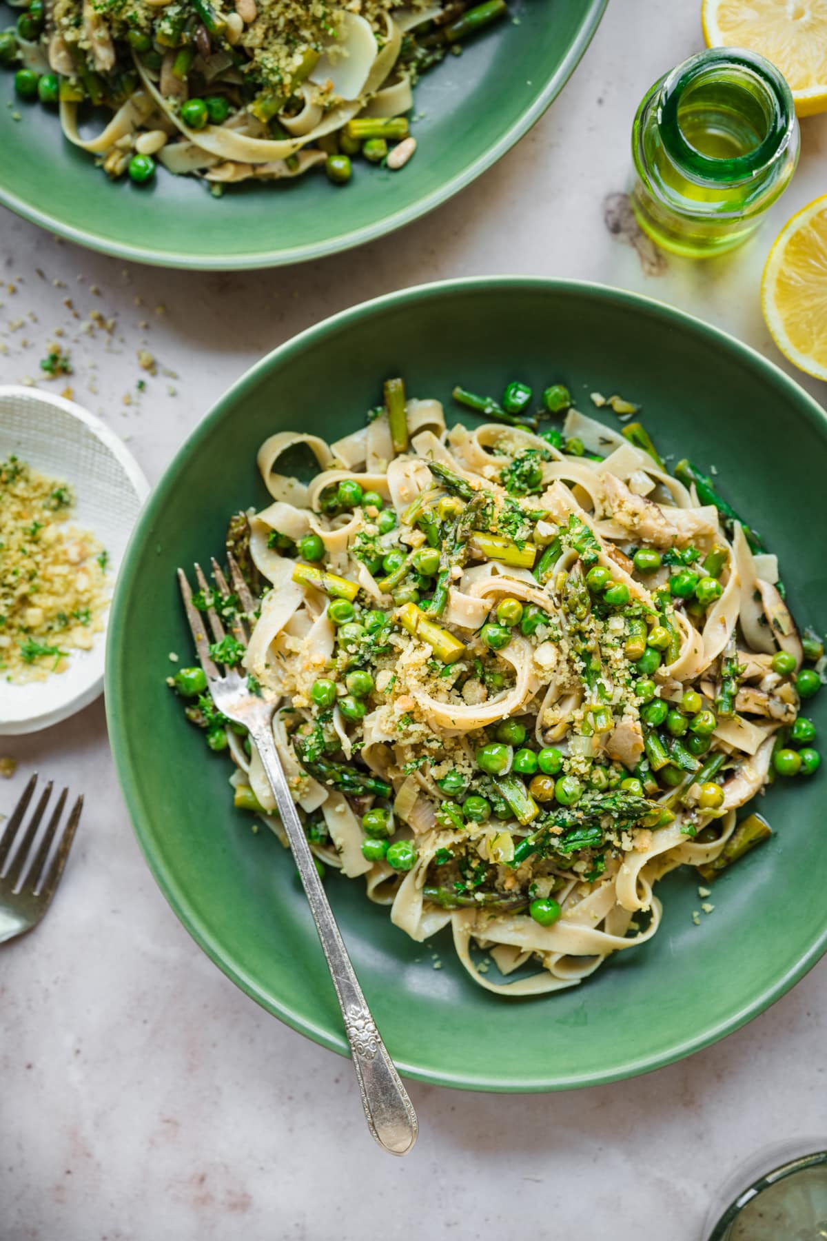 close up view of vegan spring vegetable pasta plated in a green bowl with breadcrumb topping. 