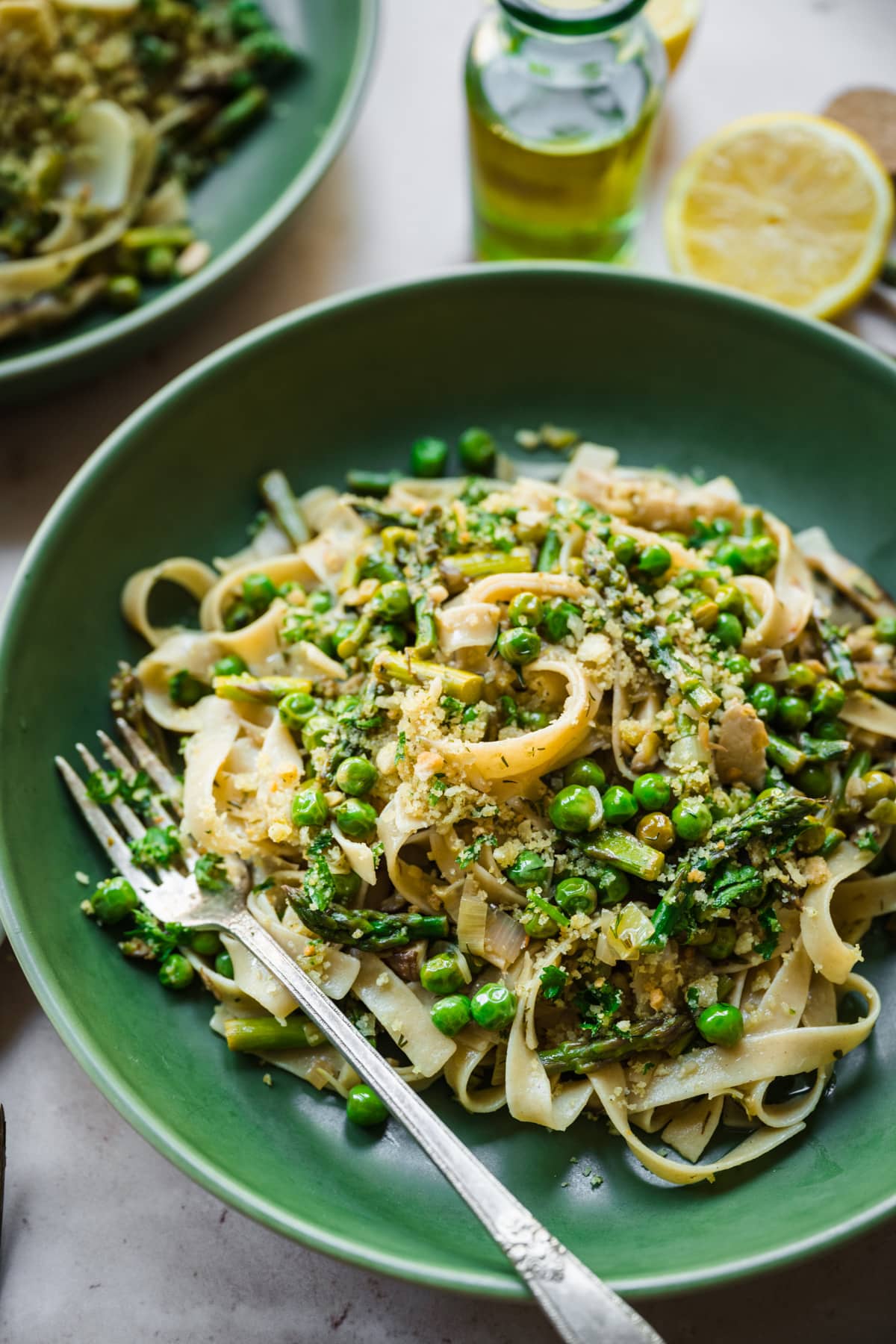 close up view of vegan spring vegetable pasta plated in a green bowl with breadcrumb topping. 