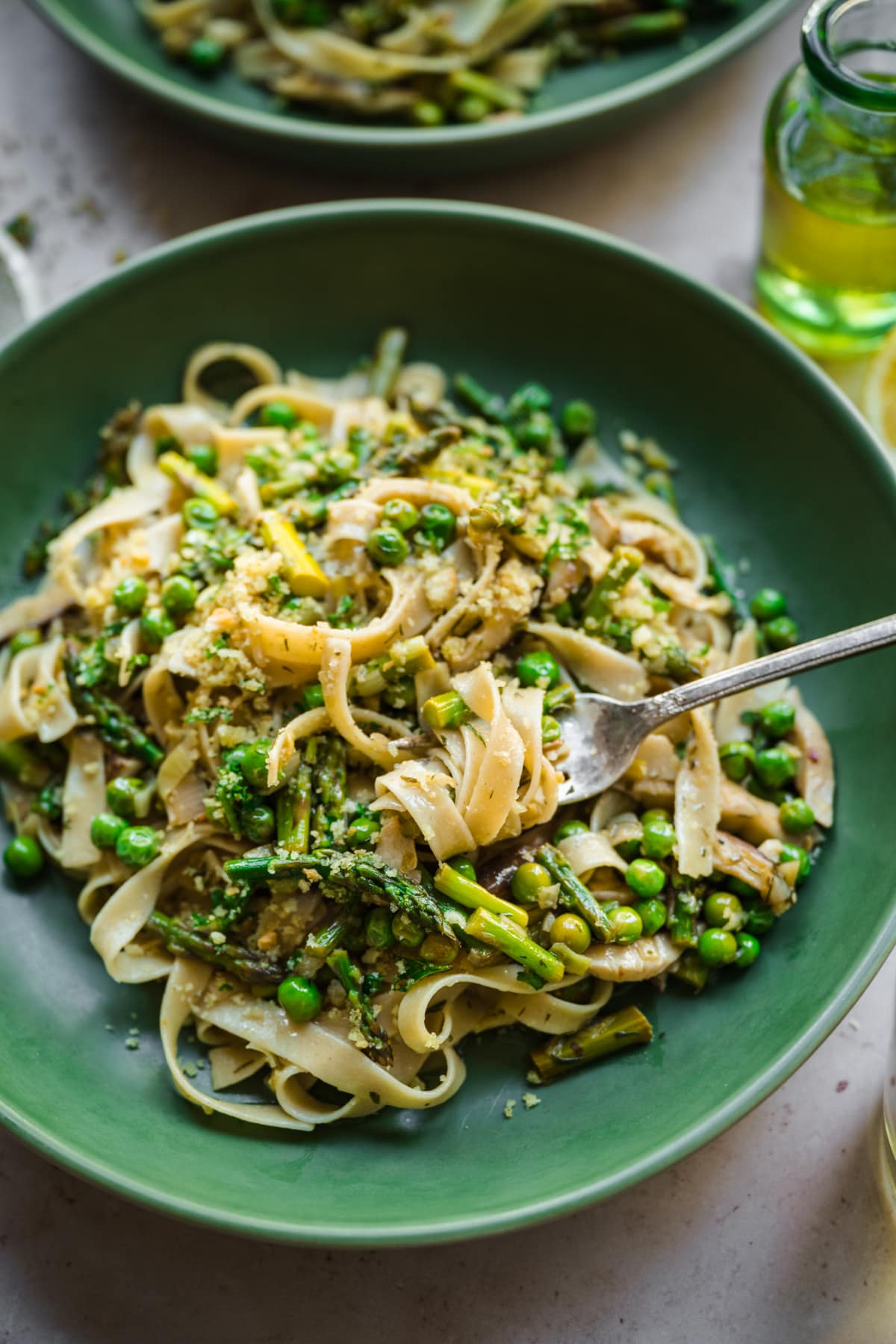 close up view of vegan spring vegetable pasta plated in a green bowl with breadcrumb topping. 