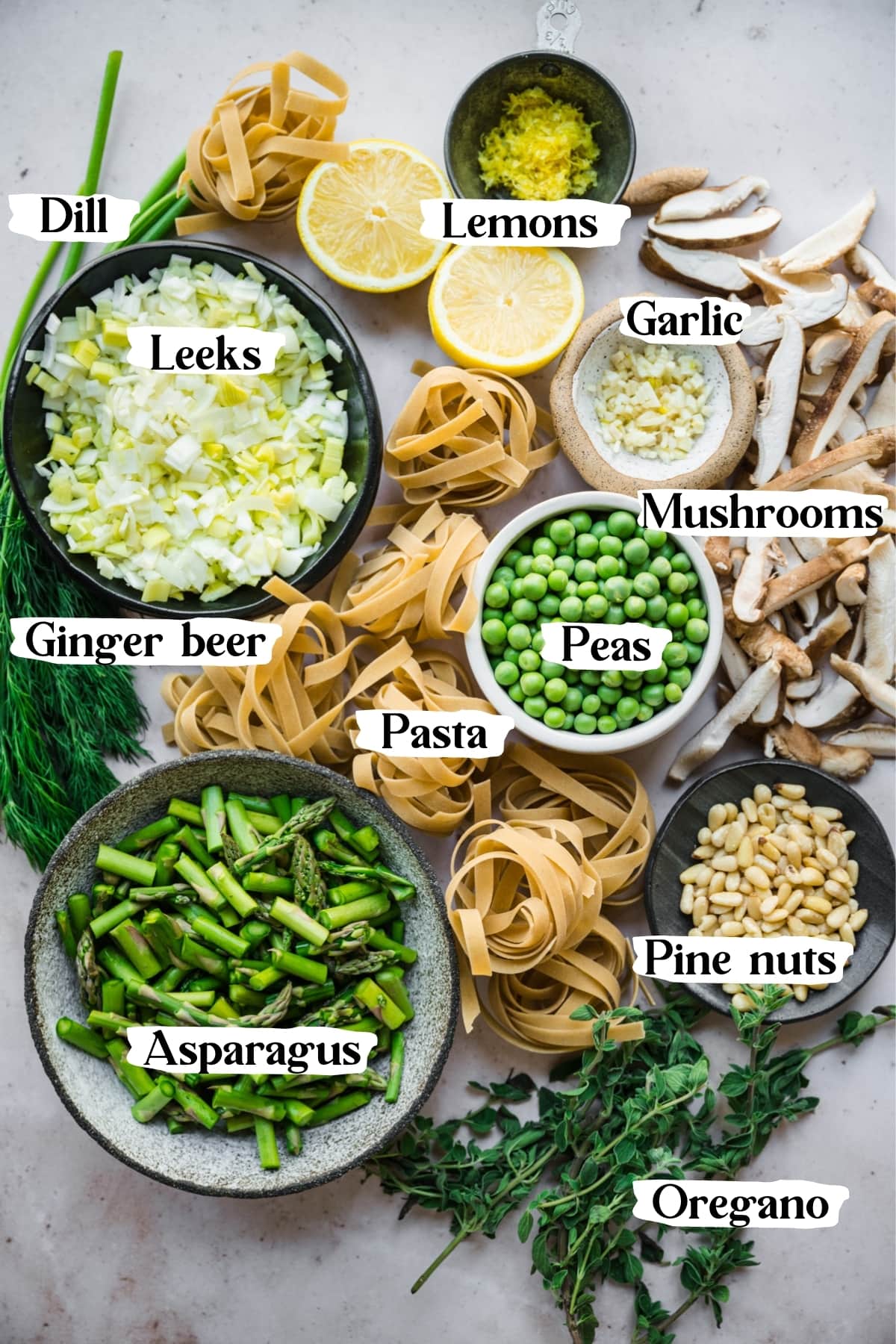 overhead view of ingredients for vegan spring vegetable pasta in small bowls with text labels. 