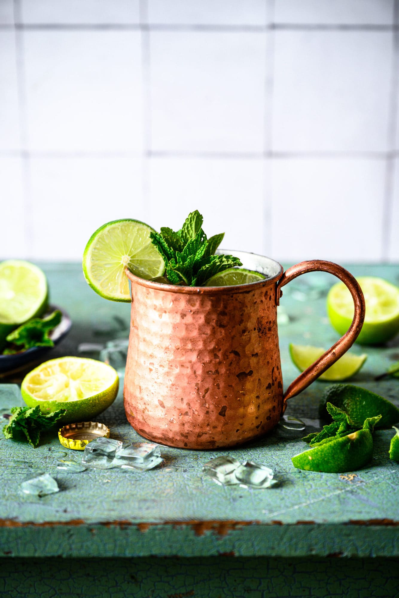 One tequila mule cocktail in copper mug with lime and mint garnish on antique blue table. 
