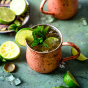 Two tequila mule cocktails in copper mugs with lime and mint garnish on antique blue table.