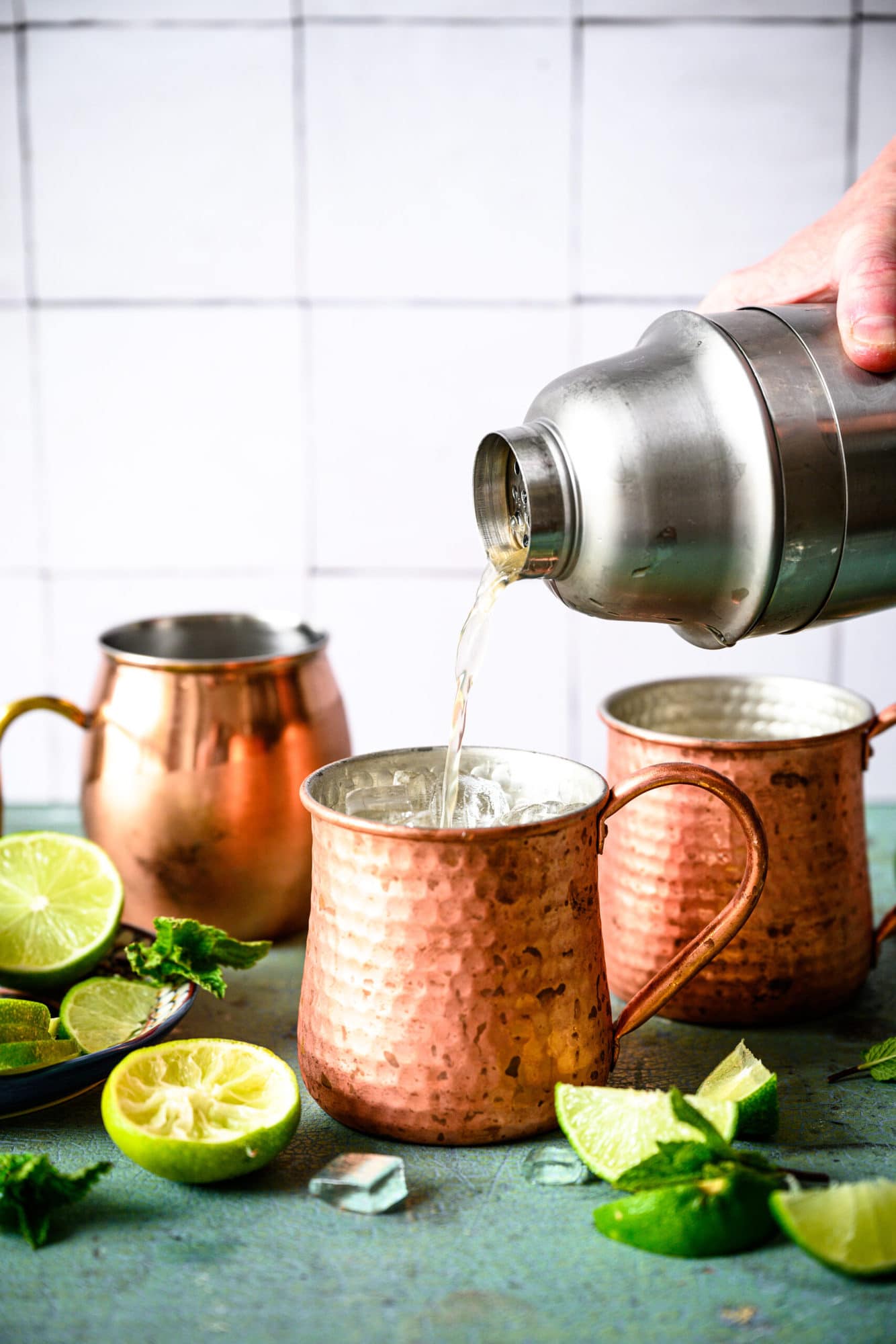 pouring tequila mule cocktail from cocktail shaker into copper mug filled with ice. 