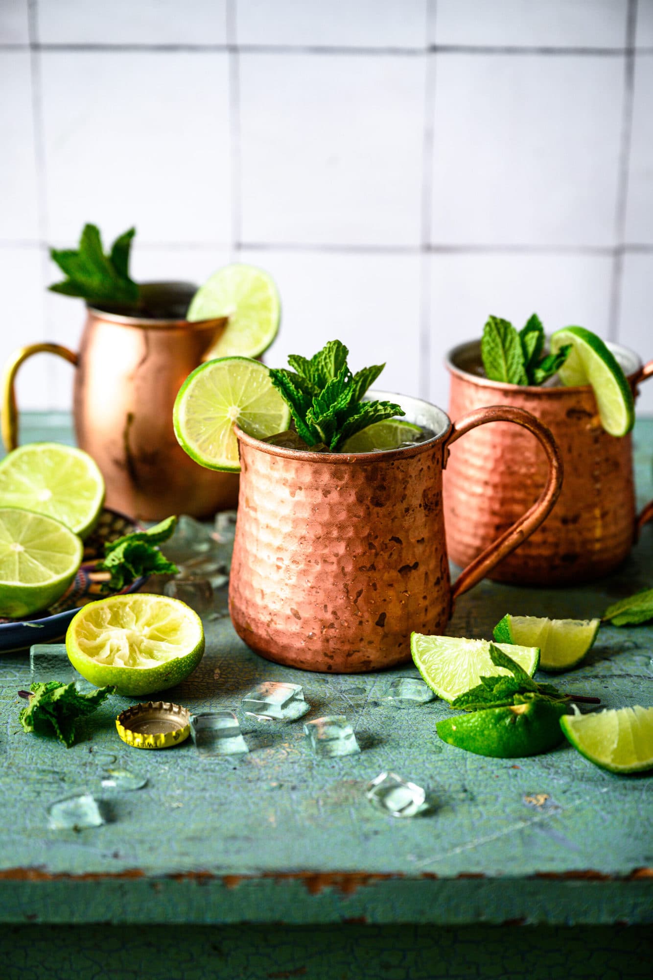 Two tequila mule cocktails in copper mugs with lime and mint garnish on antique blue table. 