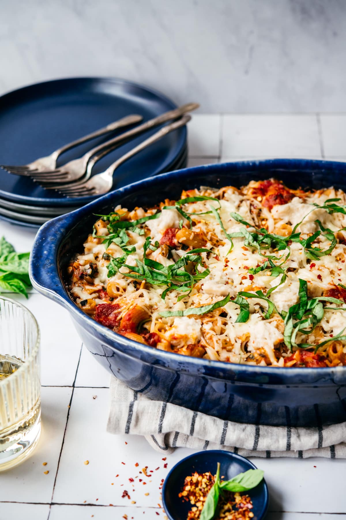 side view of vegan pasta bake topped with cheese and basil in a blue baking dish. 