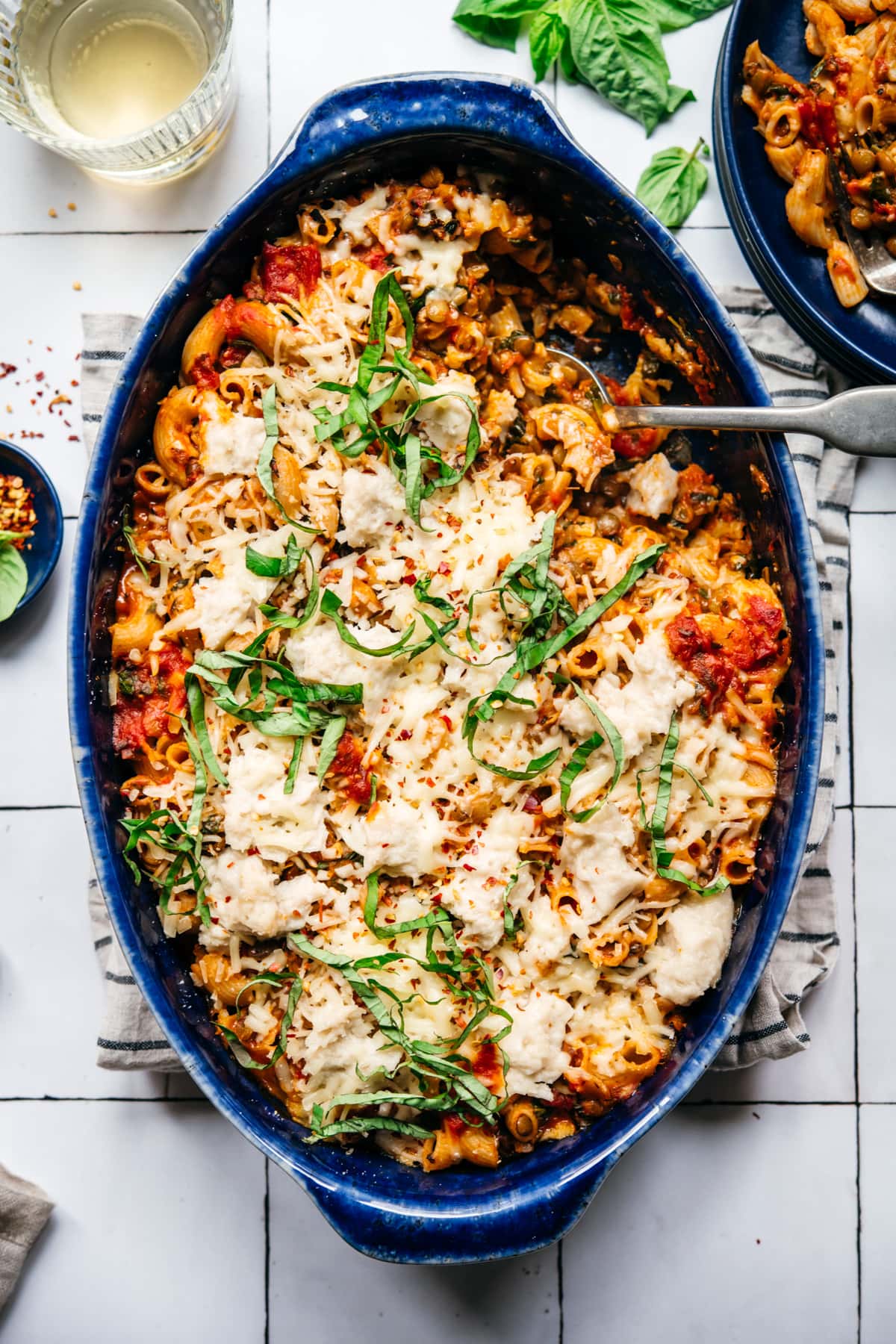 overhead view of vegan pasta bake topped with cheese and basil in a blue baking dish. 