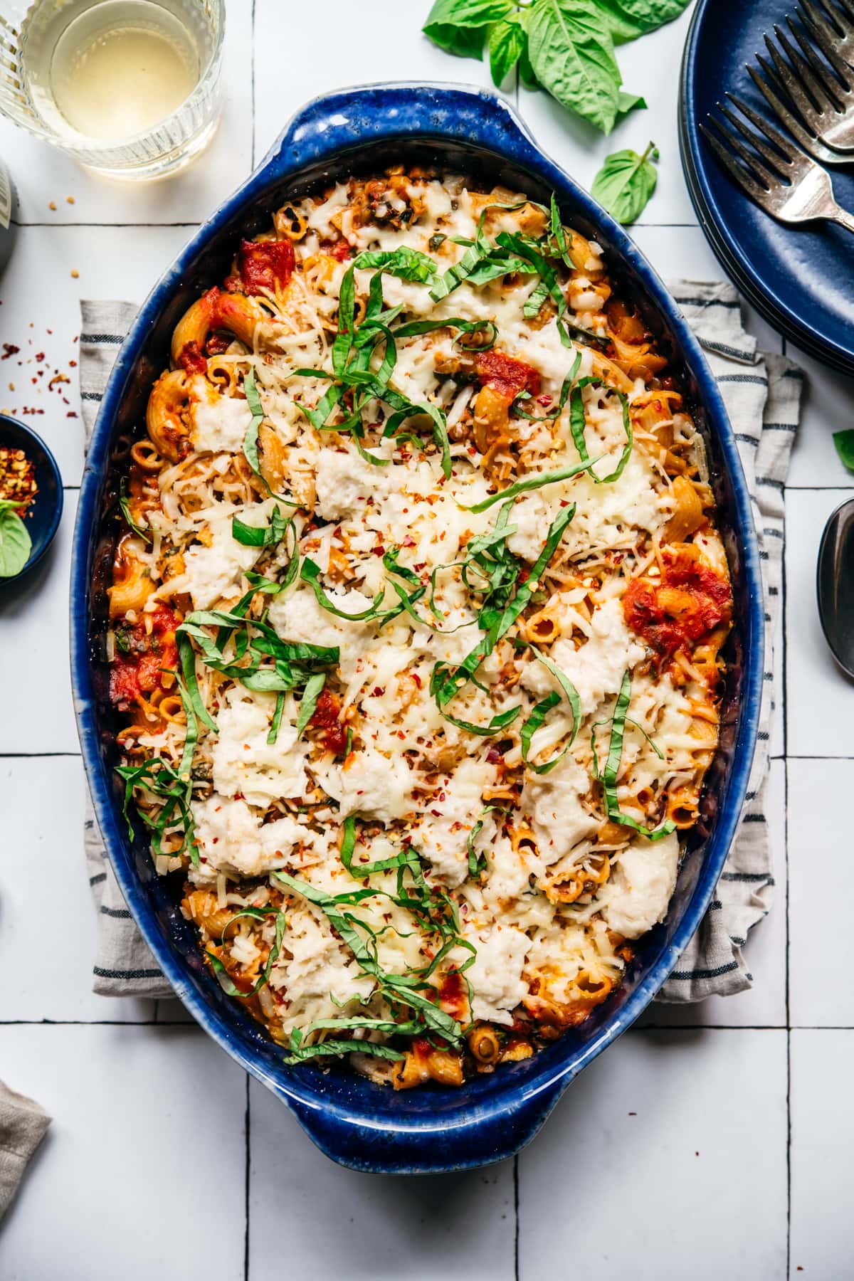 overhead view of vegan pasta bake topped with cheese and basil in a blue baking dish. 