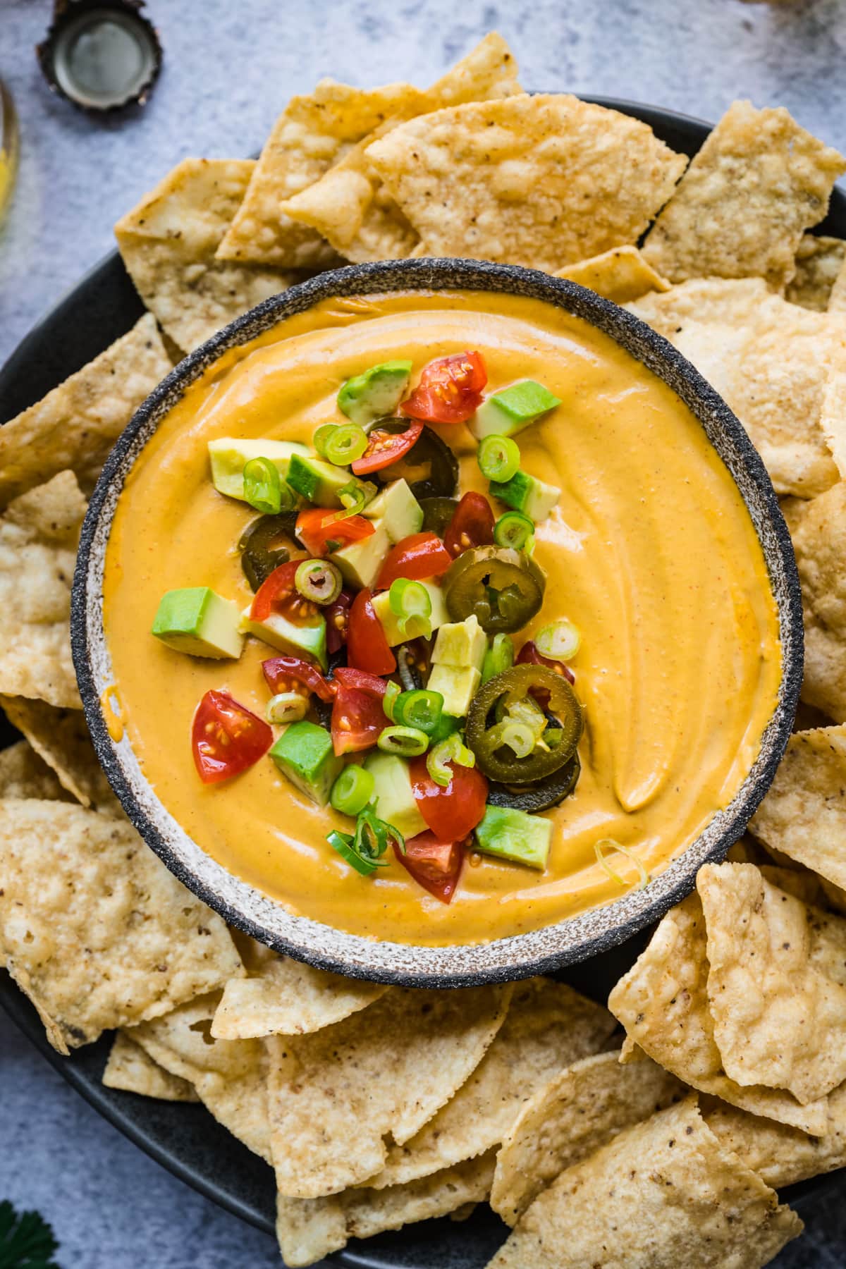 close up overhead view of vegan queso dip in a bowl with tortilla chips around it. 