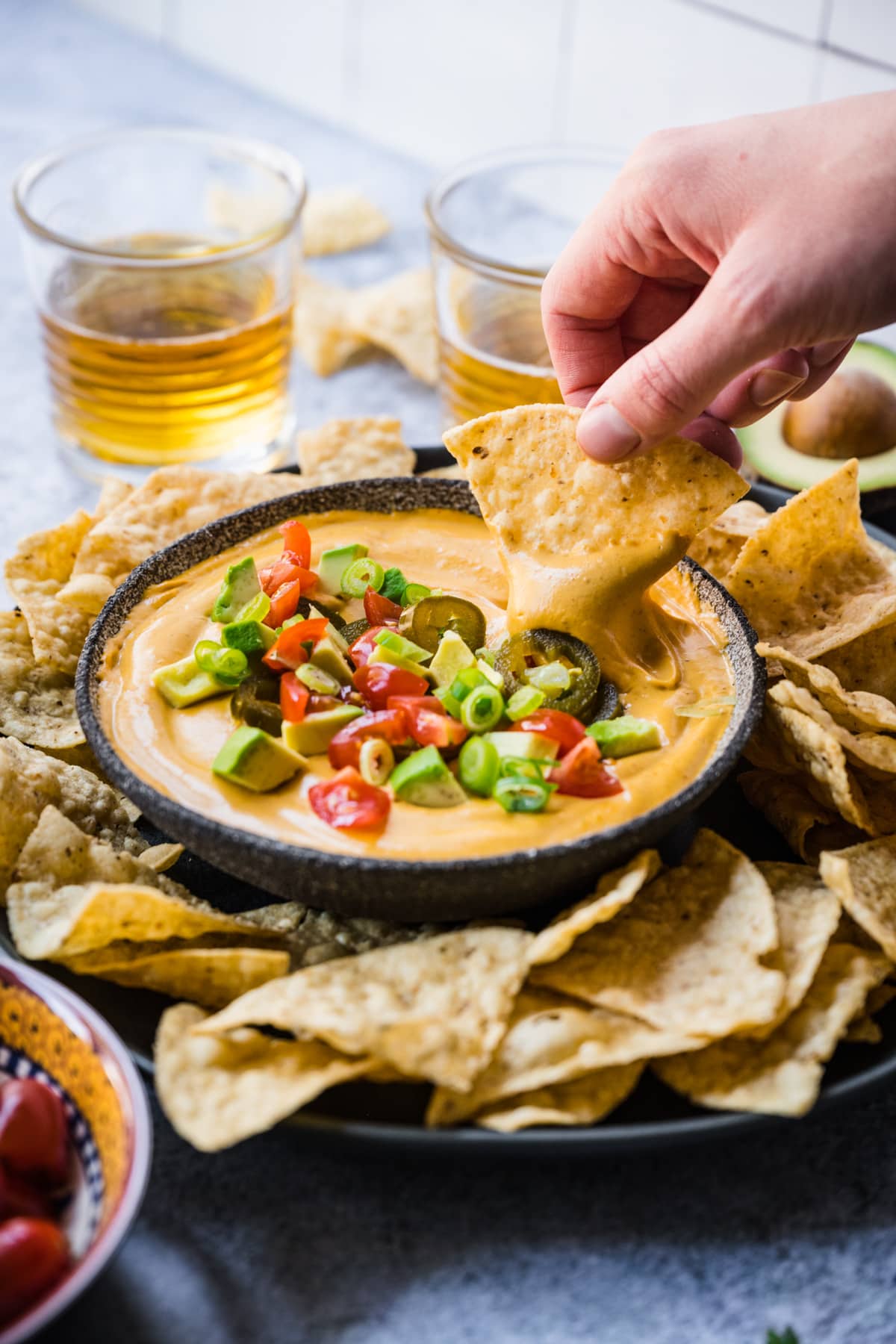person dipping tortilla chip into vegan queso dip.